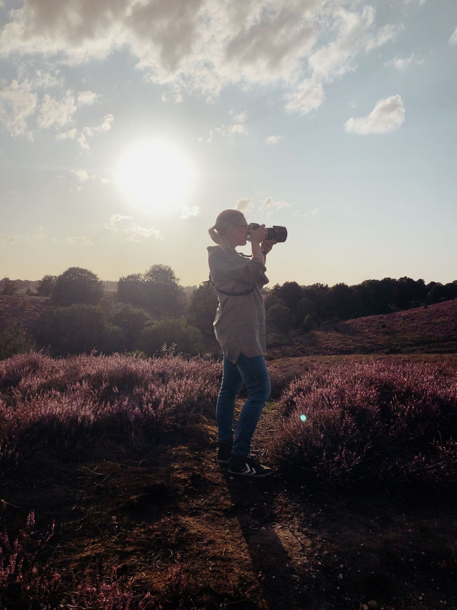 Silhouette of Marjolein photographing a purple heather field at golden sunset.
