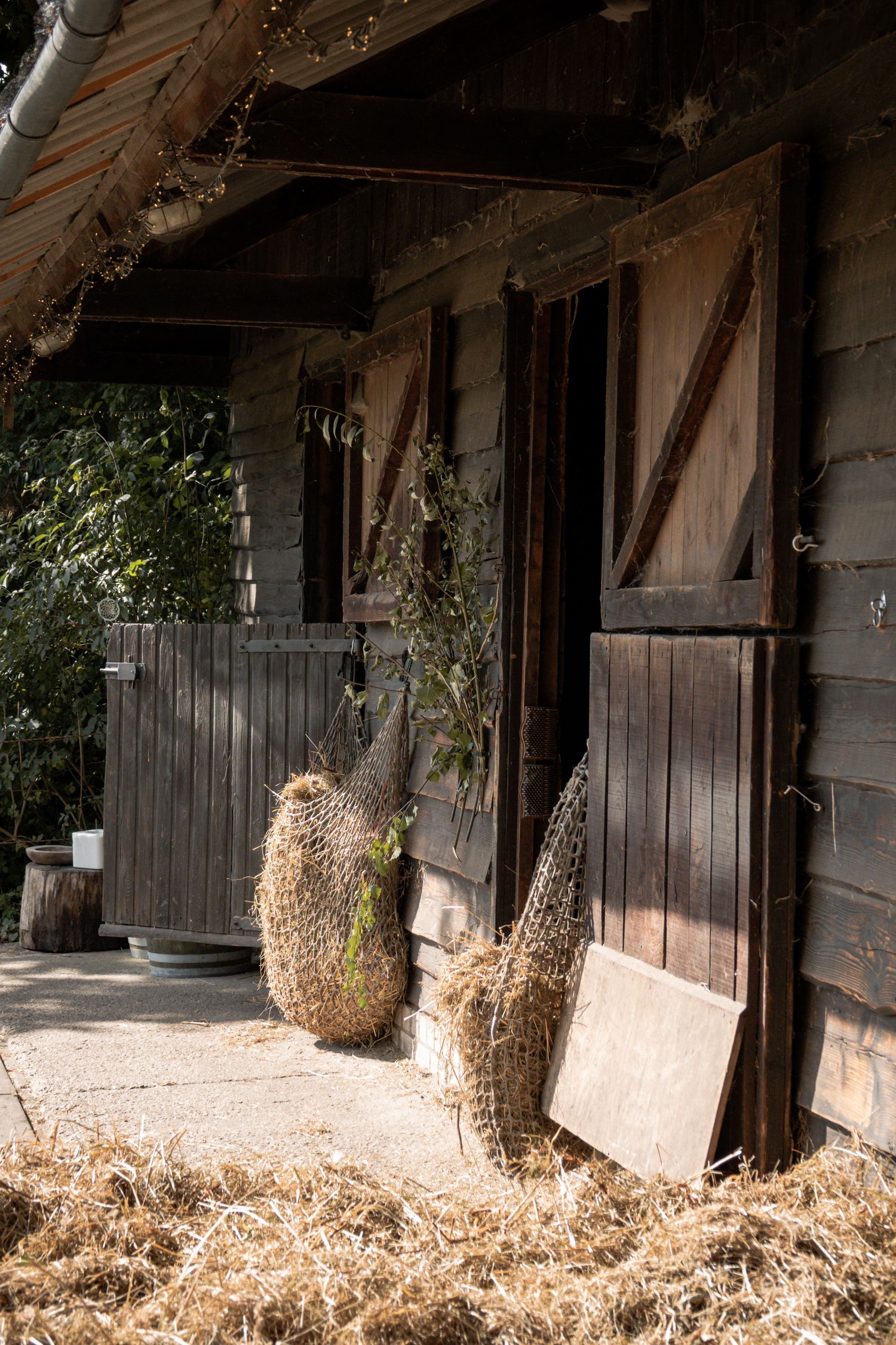 Rustic wooden stable exterior with hay bales and woven baskets in warm afternoon sunlight.