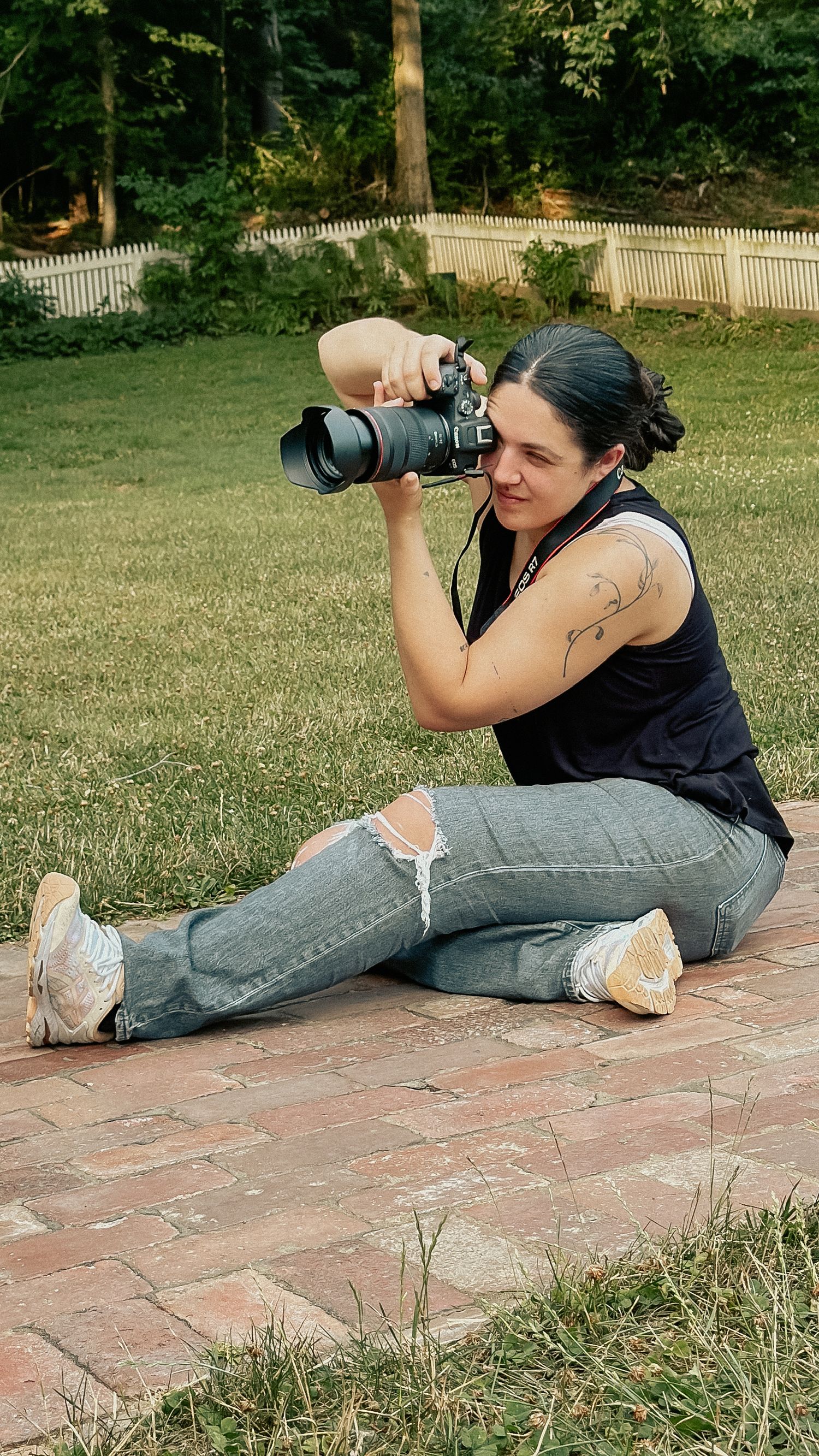 Photographer sitting on brick patio taking photos with professional camera.
