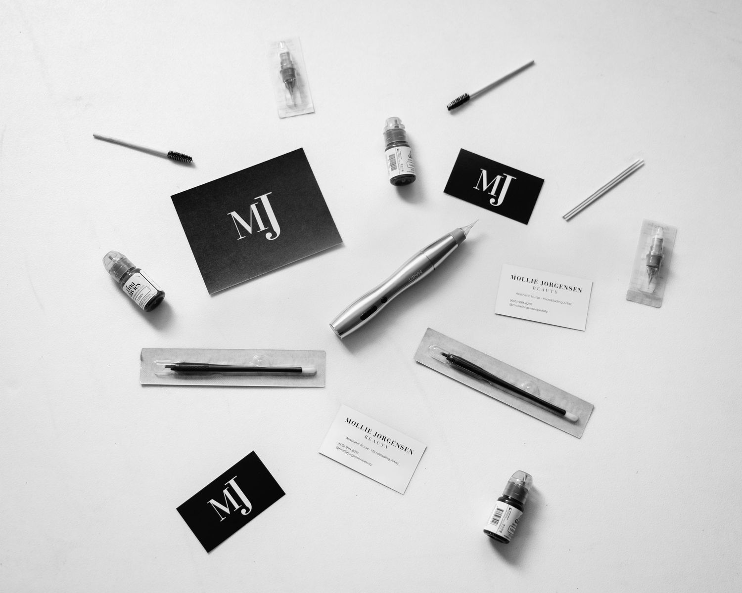Minimalist black and white flatlay of cosmetic bottles and business cards arranged on white surface.