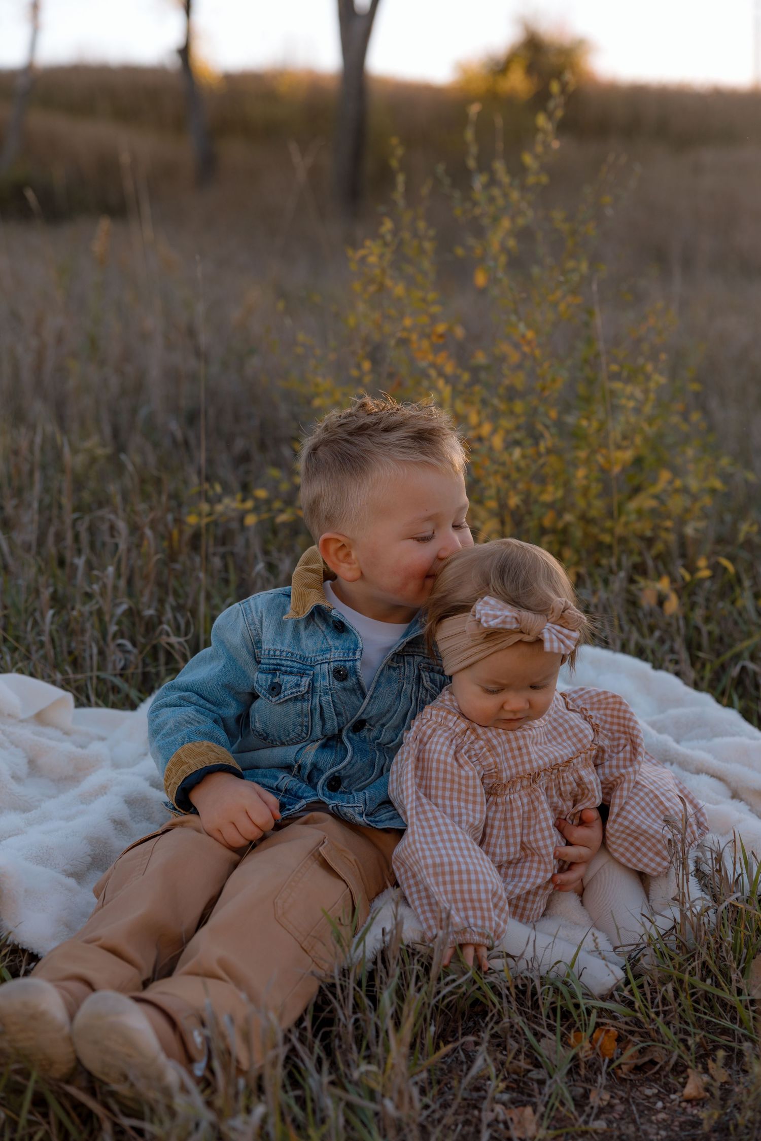 Two children lying on a white blanket in a field with yellow wildflowers during golden hour.