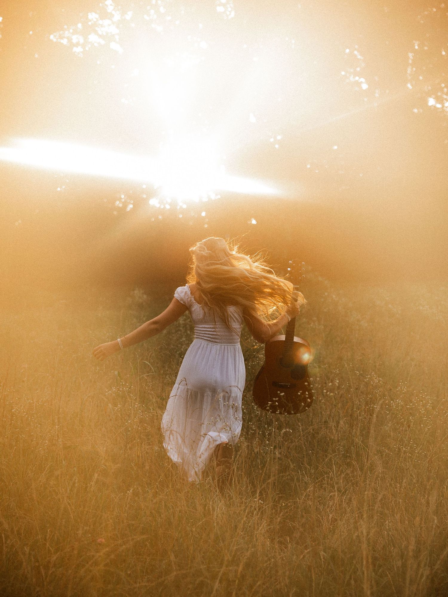 Woman with acoustic guitar in wildflowers at sunset