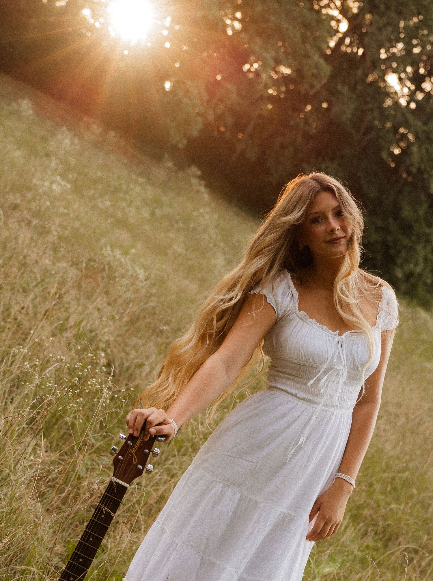 Woman with acoustic guitar in wildflowers at sunset