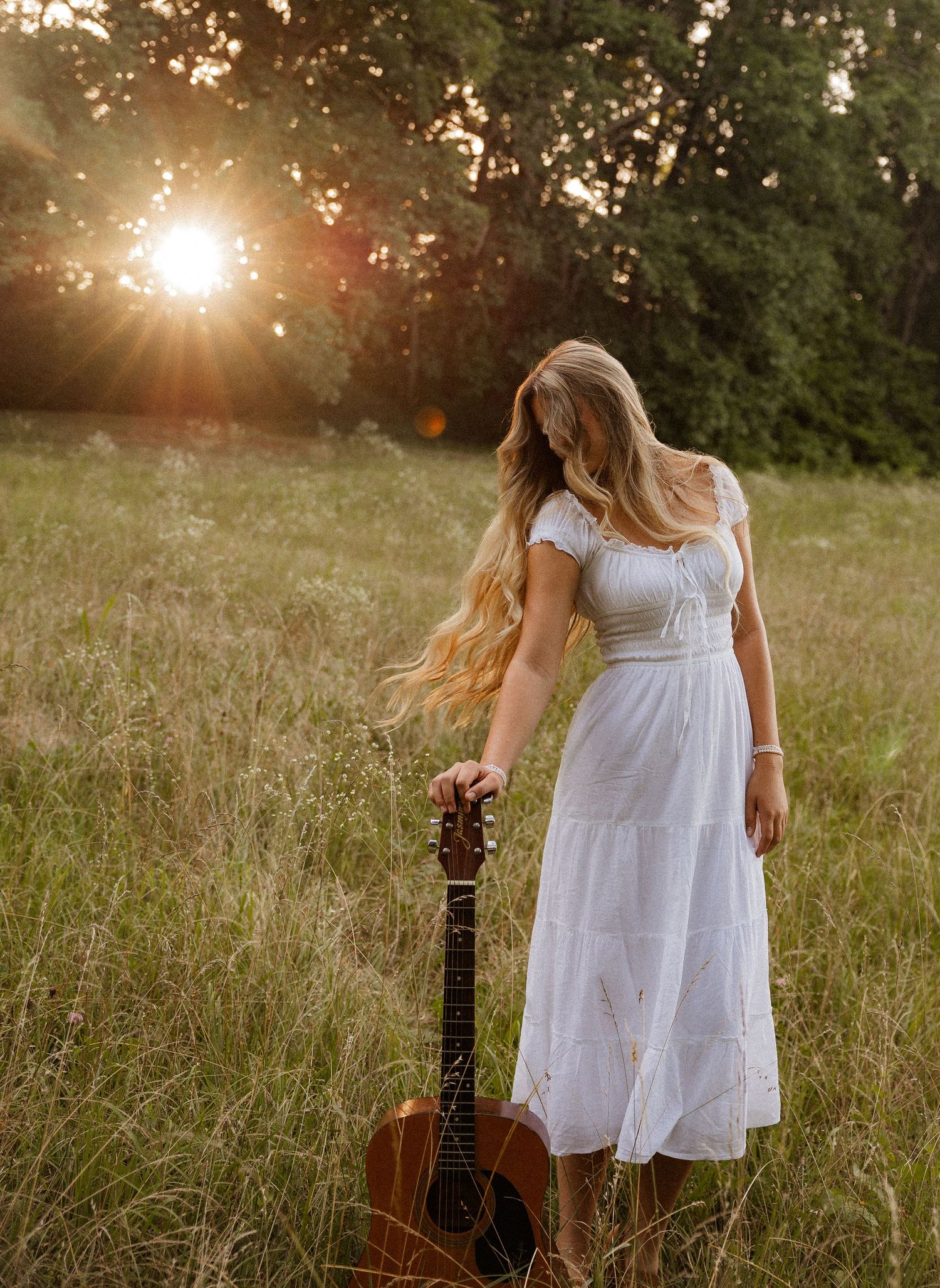 Woman with acoustic guitar in wildflowers at sunset