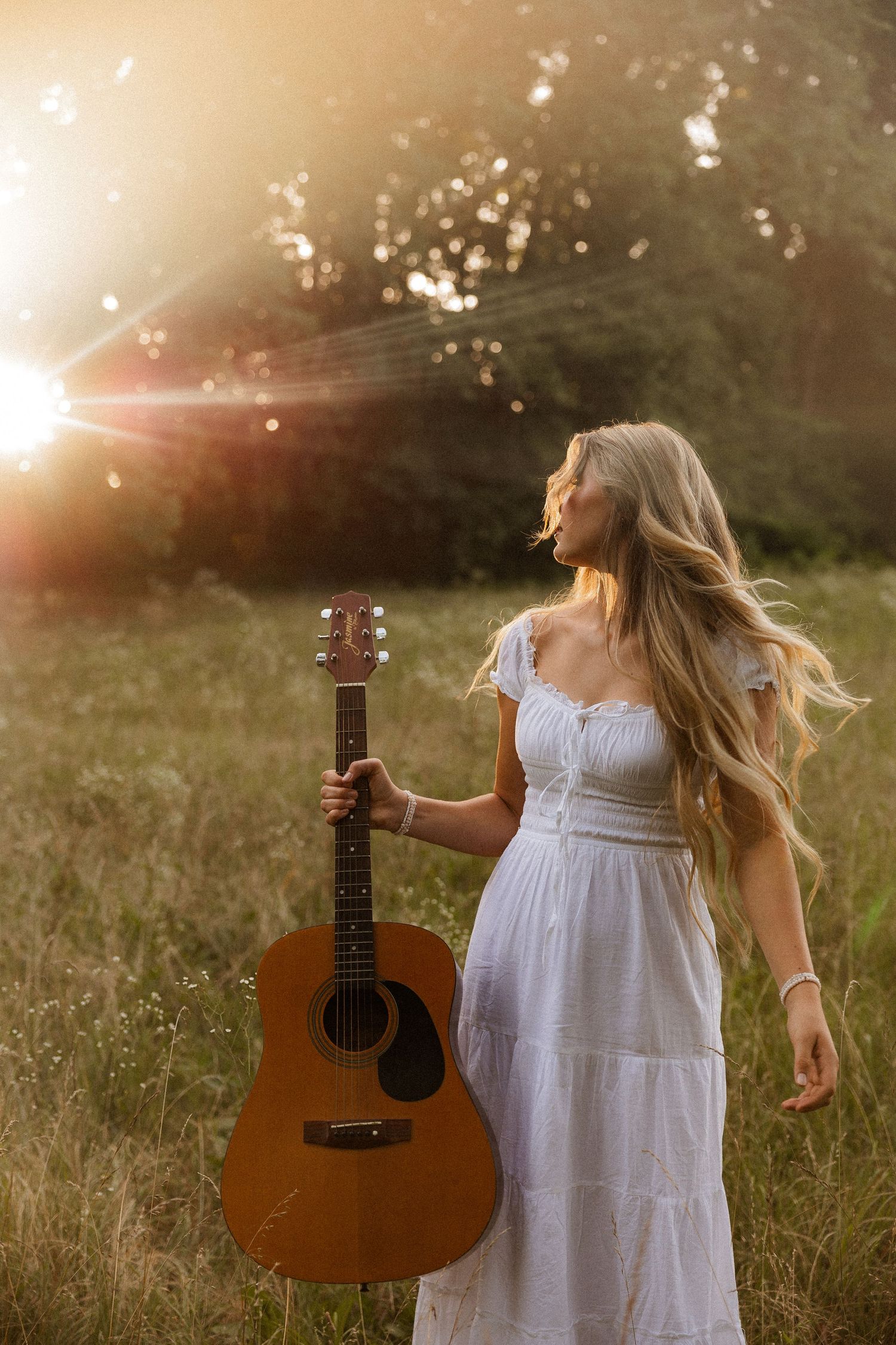 Woman with acoustic guitar in wildflowers at sunset