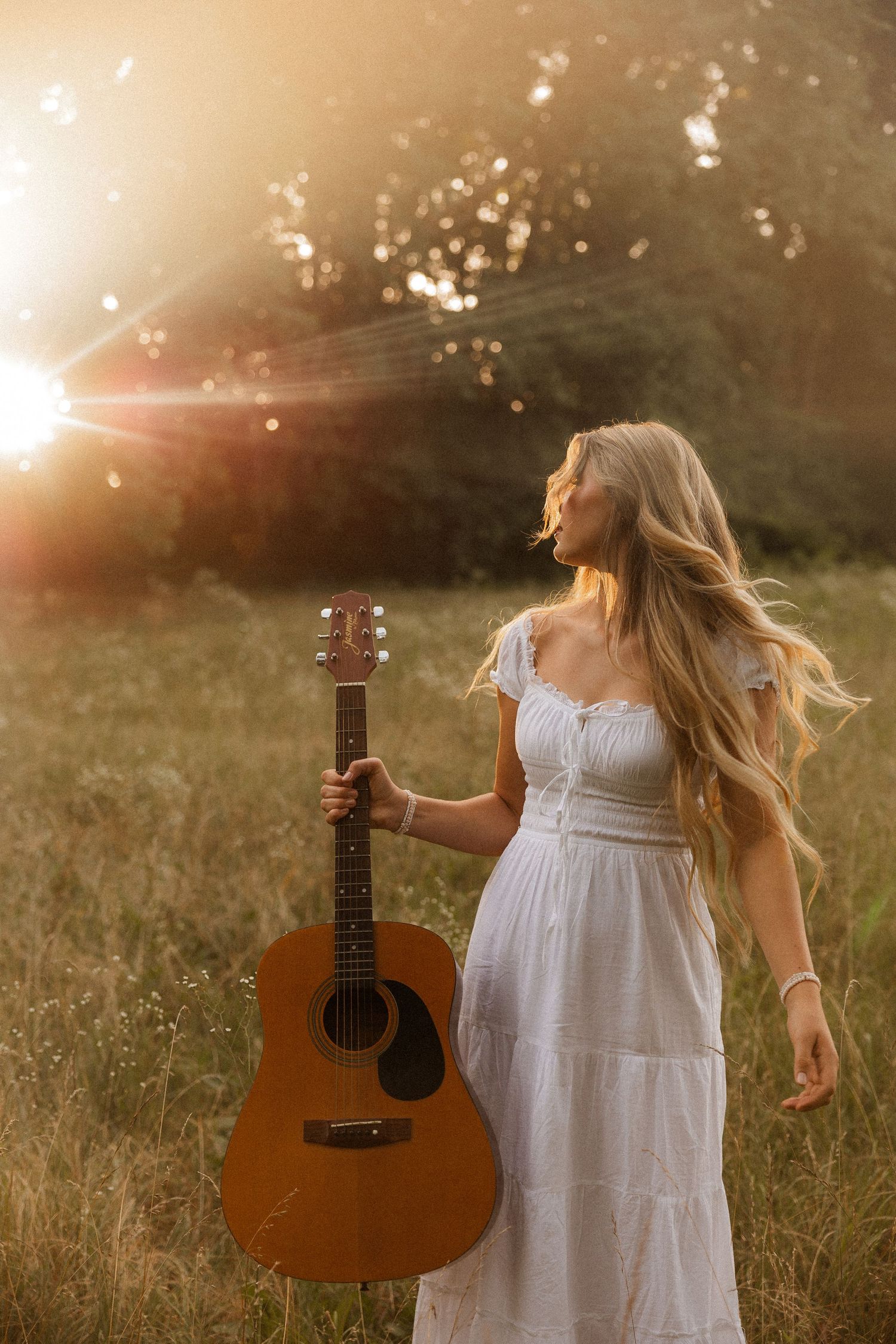 Woman with acoustic guitar in wildflowers at sunset