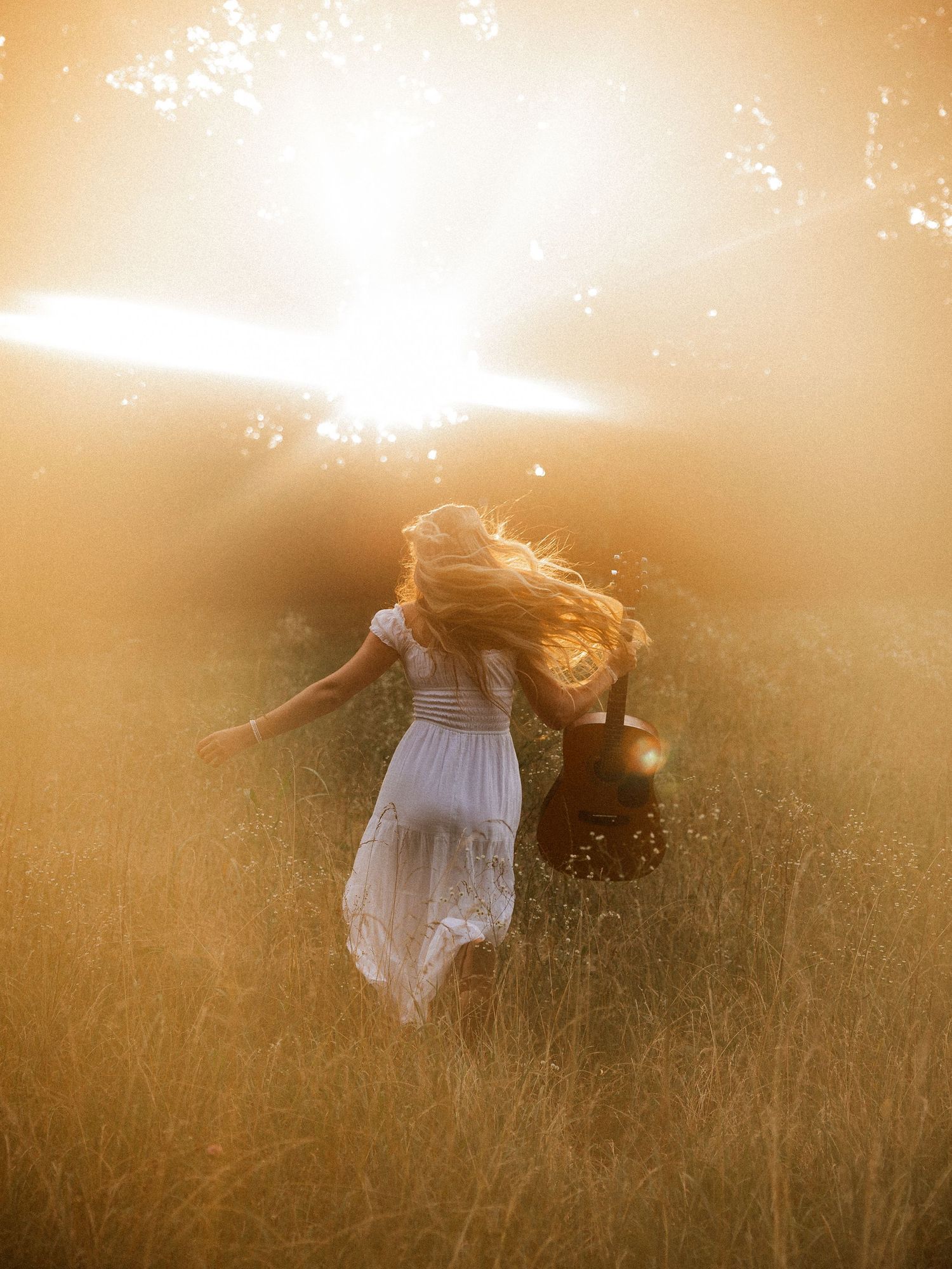 Woman with acoustic guitar in wildflowers at sunset