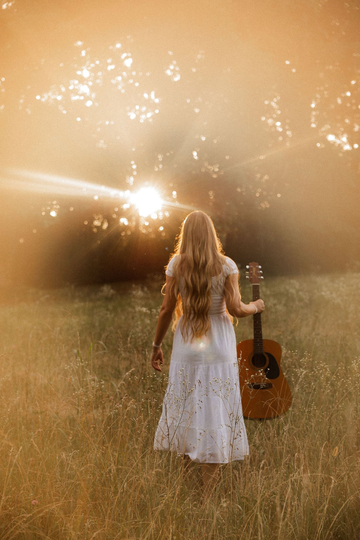 Woman with acoustic guitar in wildflowers at sunset