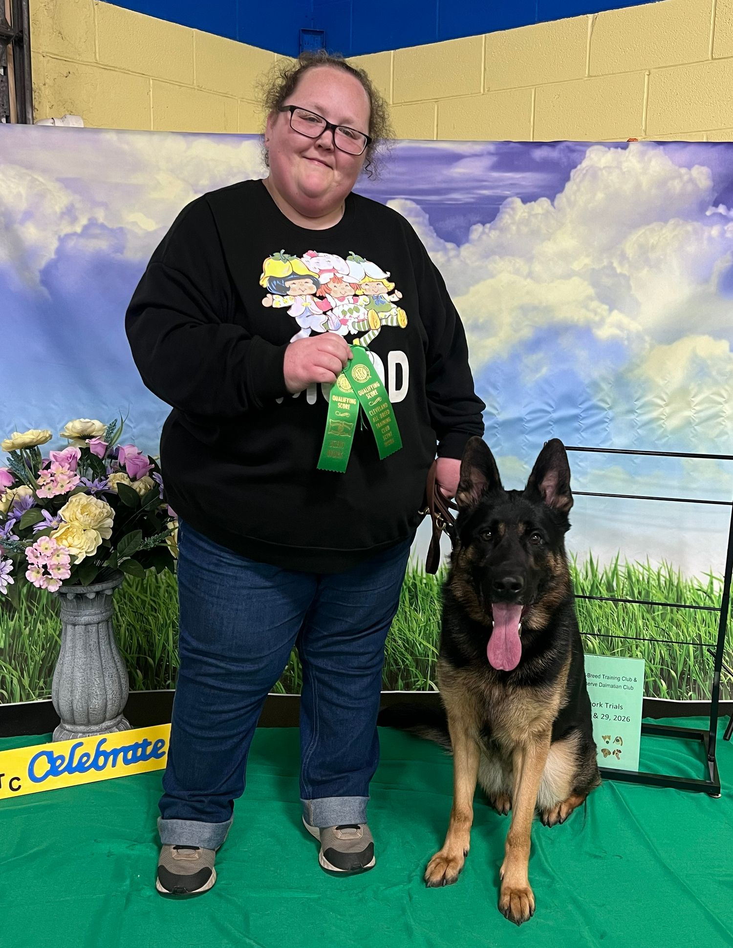 Handler posing with a black dog and ribbons after a dog event.
