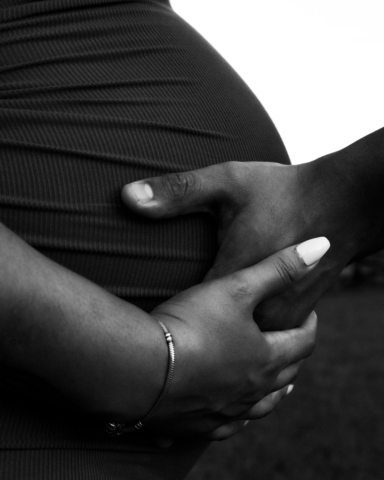 Black and white photo of a pregnant woman cradling her baby bump with both hands, wearing a bracelet.