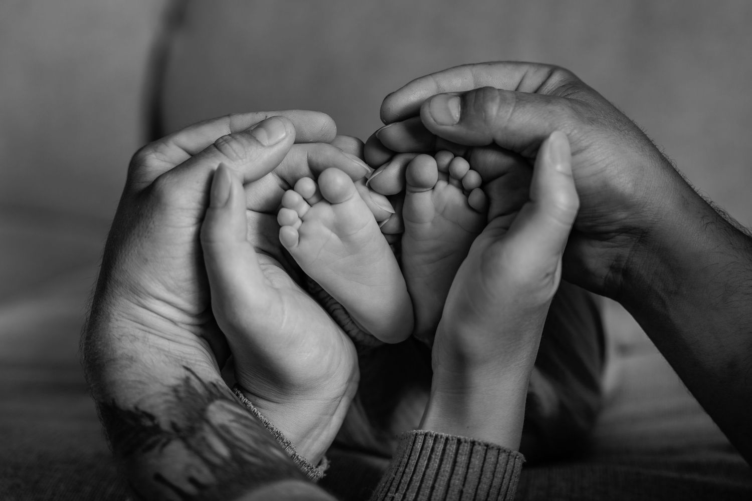 Black and white photo of parents cradling tiny newborn baby feet in their hands.