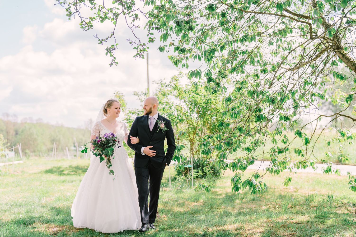 Bride and groom walking together under blooming tree on sunny spring wedding day.