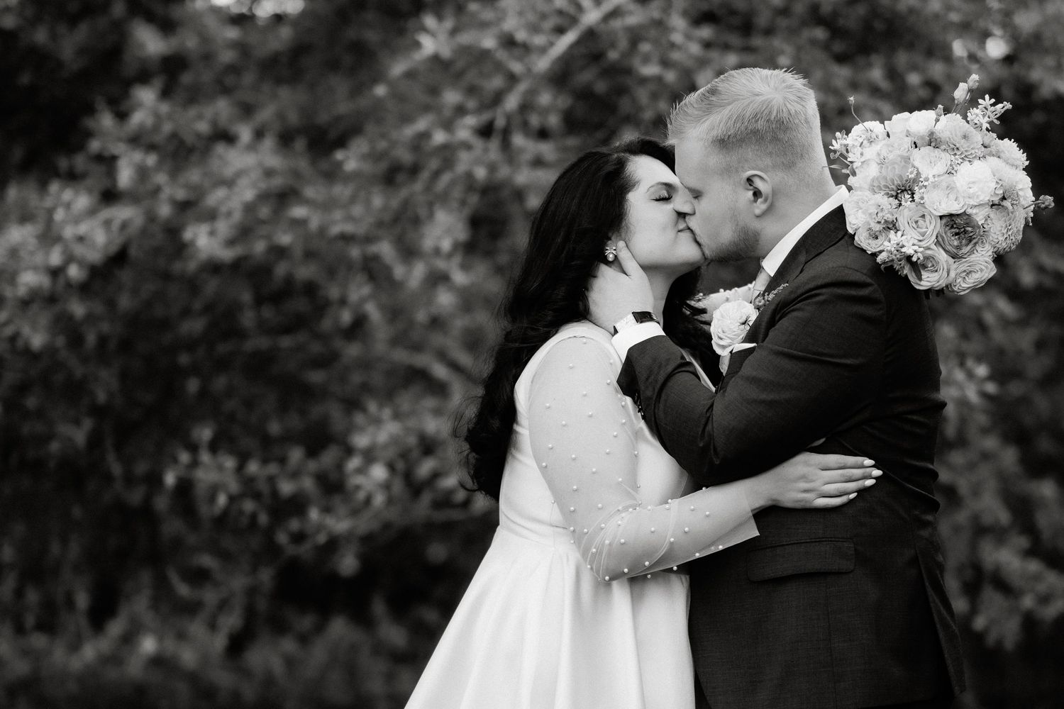 Black and white photo of bride and groom sharing a romantic kiss outdoors on their wedding day.