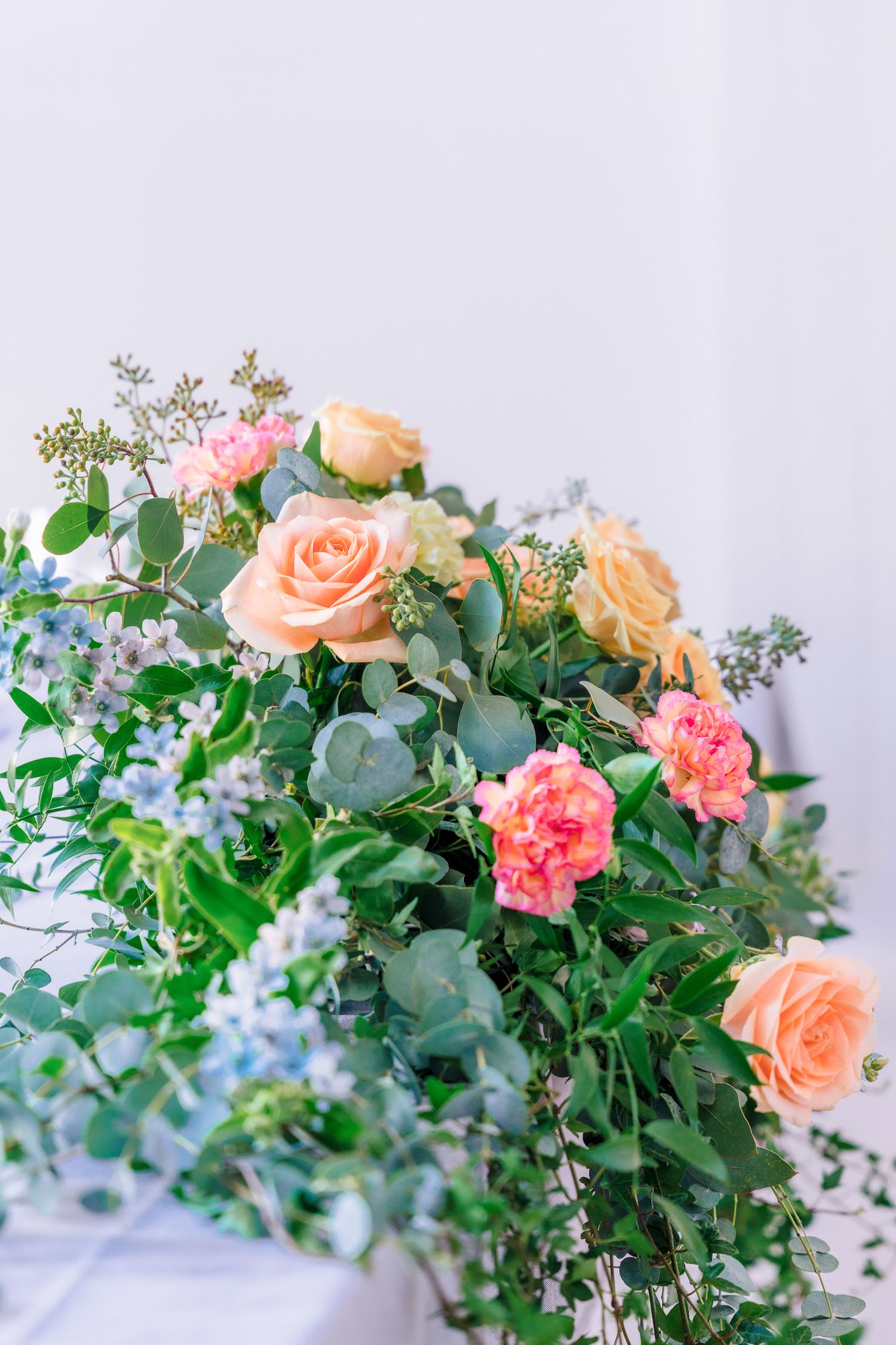 Lush floral arrangement featuring peach roses, pink carnations, and eucalyptus greenery against white background.