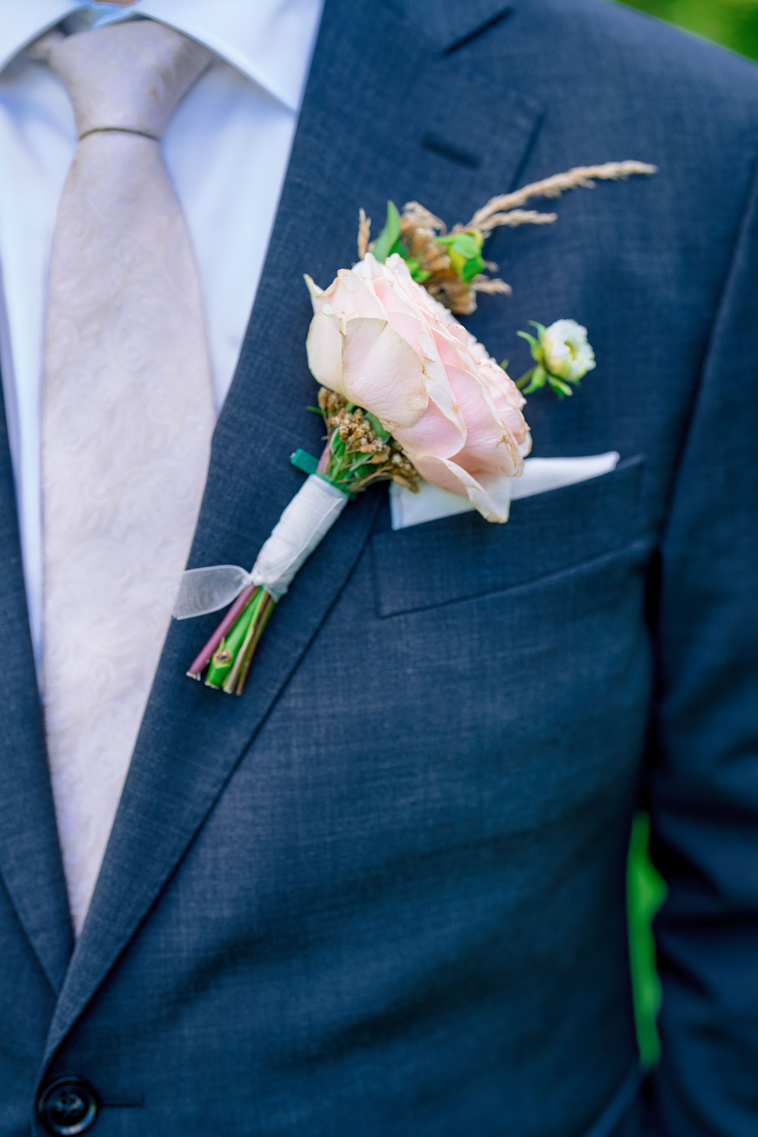 Close-up of groom's blush rose boutonniere on navy suit with gray tie.