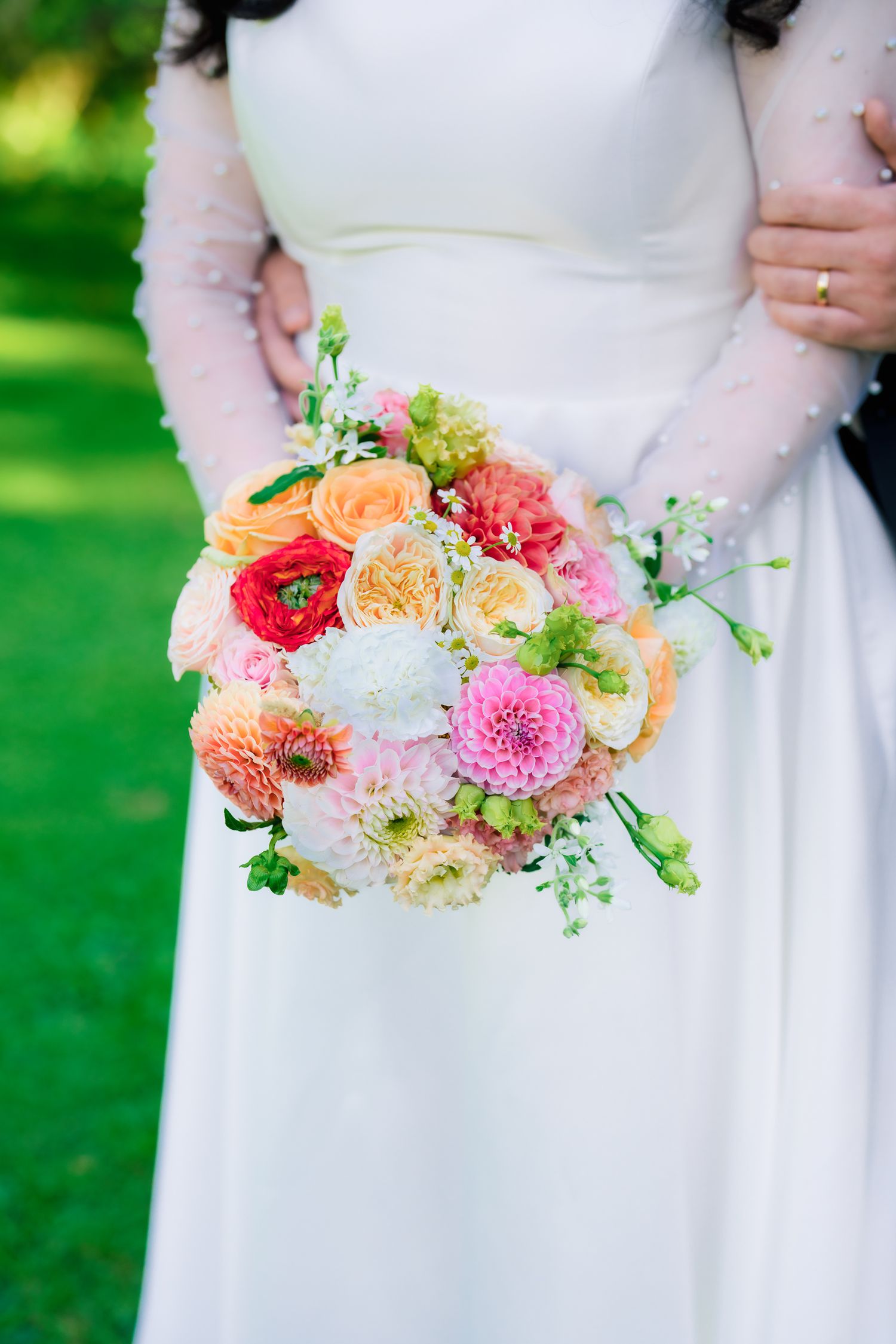 Close-up of vibrant bridal bouquet with pink dahlias, roses, and orange flowers.