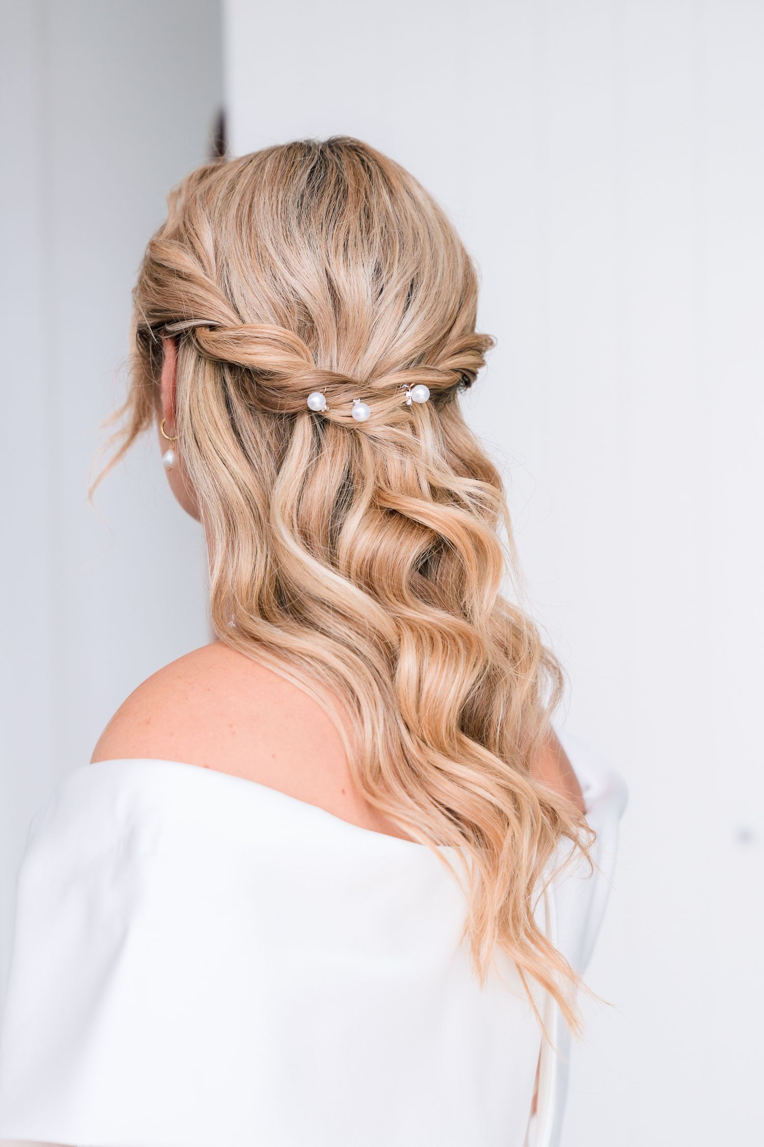 Bride's romantic half-up wavy hairstyle adorned with delicate pearl hair pins on her wedding day.