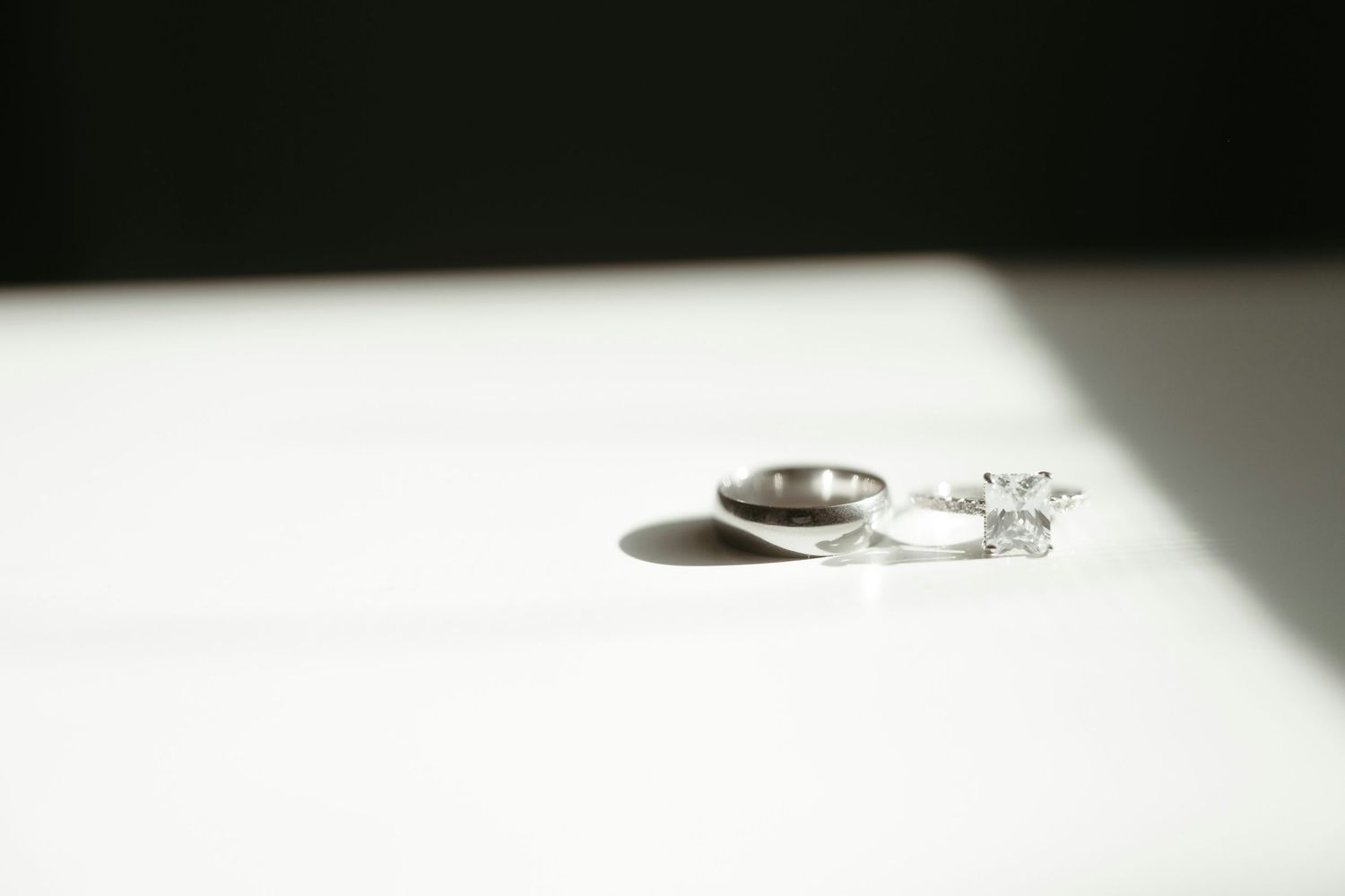 Diamond engagement ring and wedding band casting shadows on white surface.