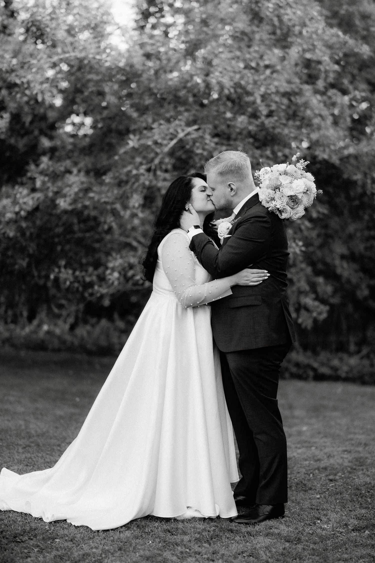 Black and white photo of bride and groom kissing in garden setting.