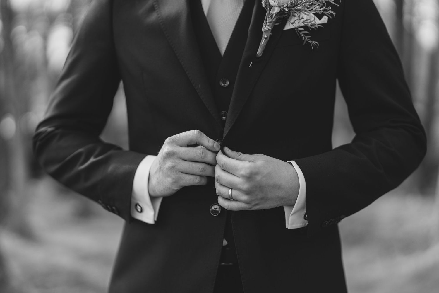 Groom in black suit adjusting jacket with boutonniere in black and white.