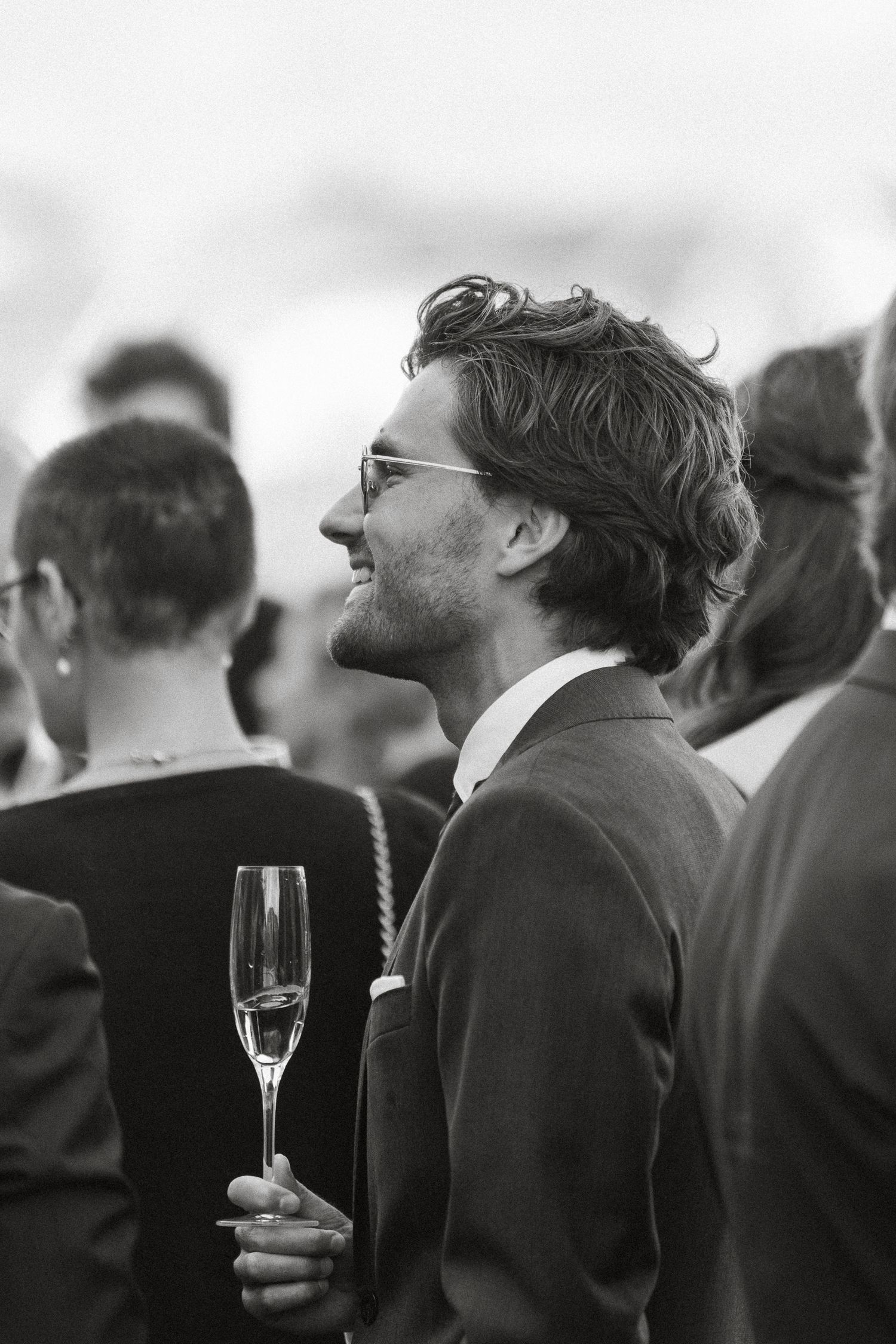 Black and white photo of a smiling man in a suit holding a champagne flute at a social gathering.