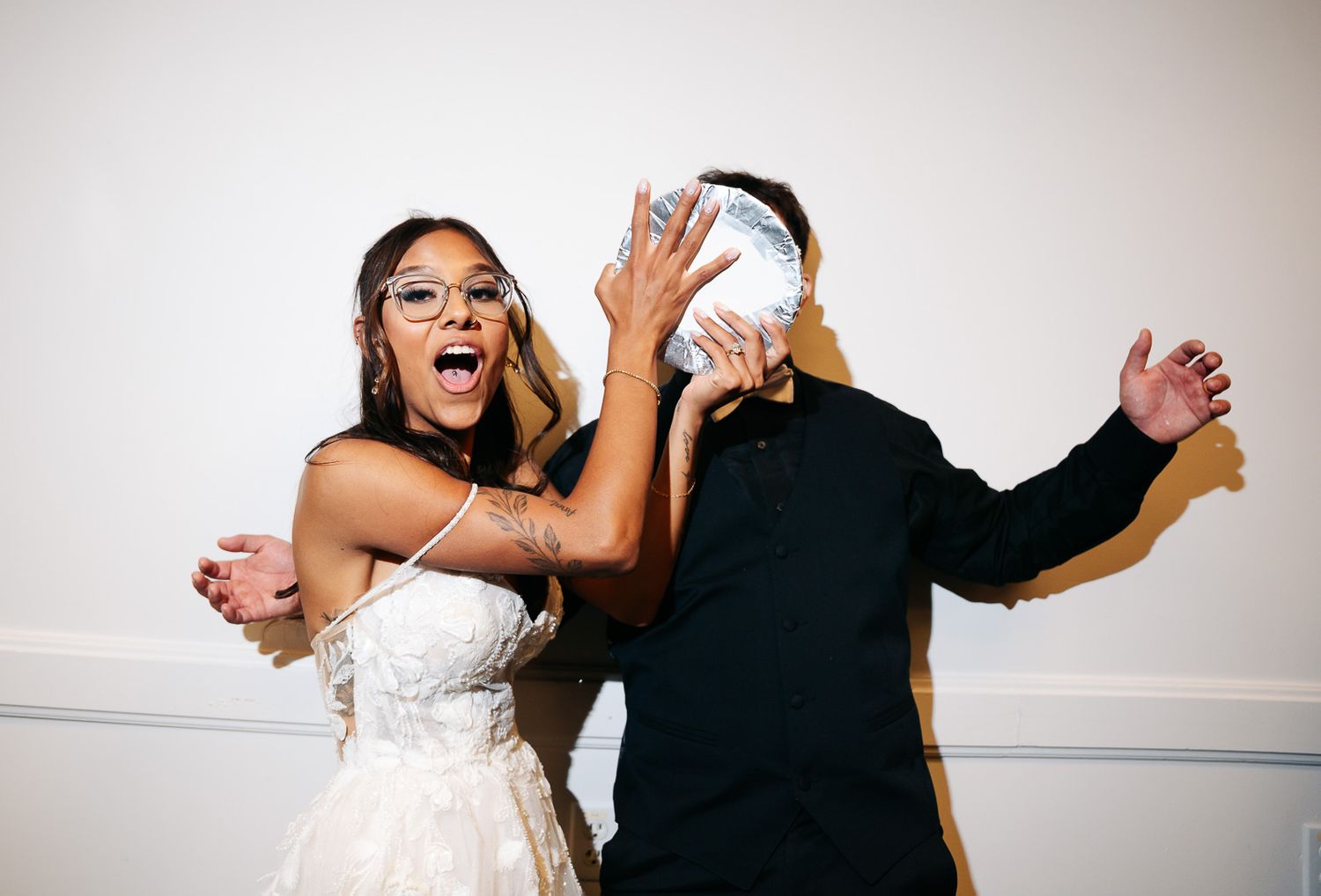 Bride in white dress and groom in black playfully pose with a mirror ball at wedding reception.