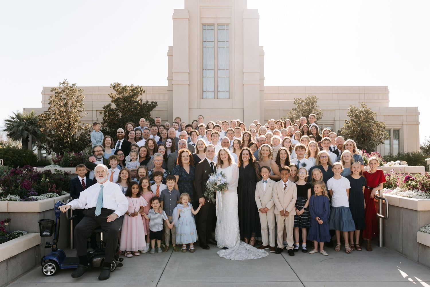 Large wedding family group photo on steps outside LDS temple on sunny day.