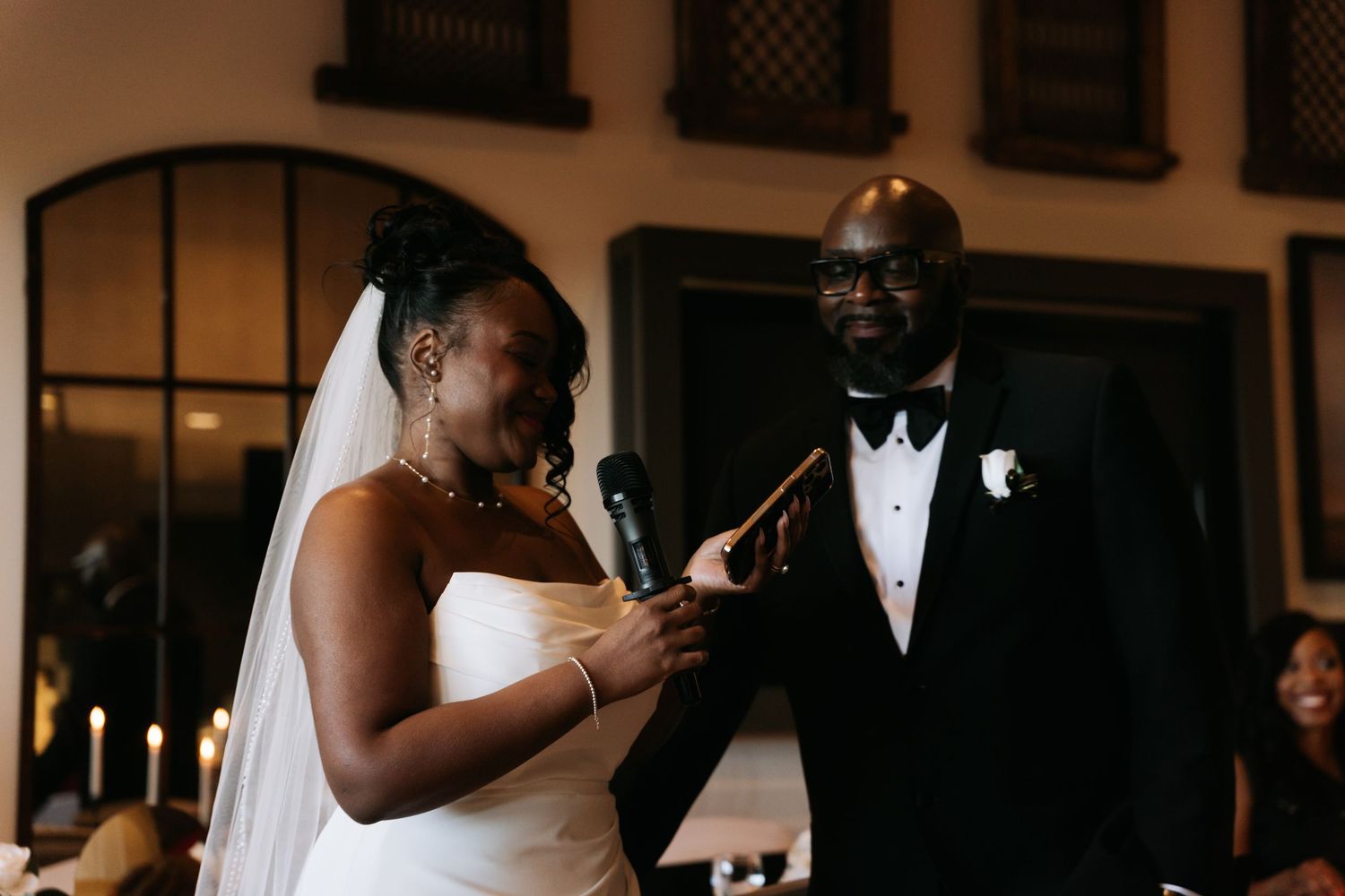 Bride in white strapless gown and veil reads vows beside groom in black tuxedo during wedding ceremony.
