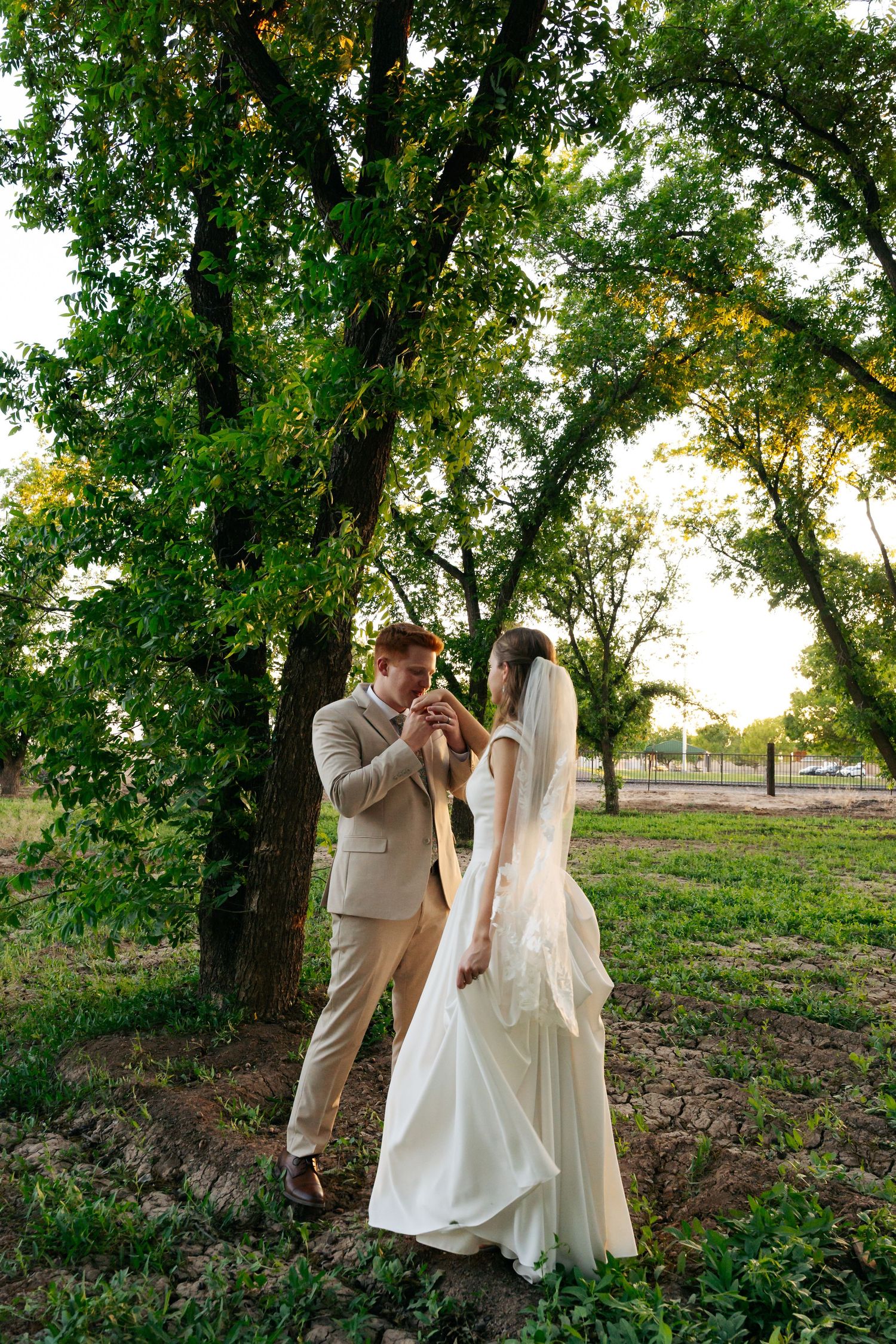 Bride and groom share a romantic moment among lush green trees during outdoor wedding photo session.