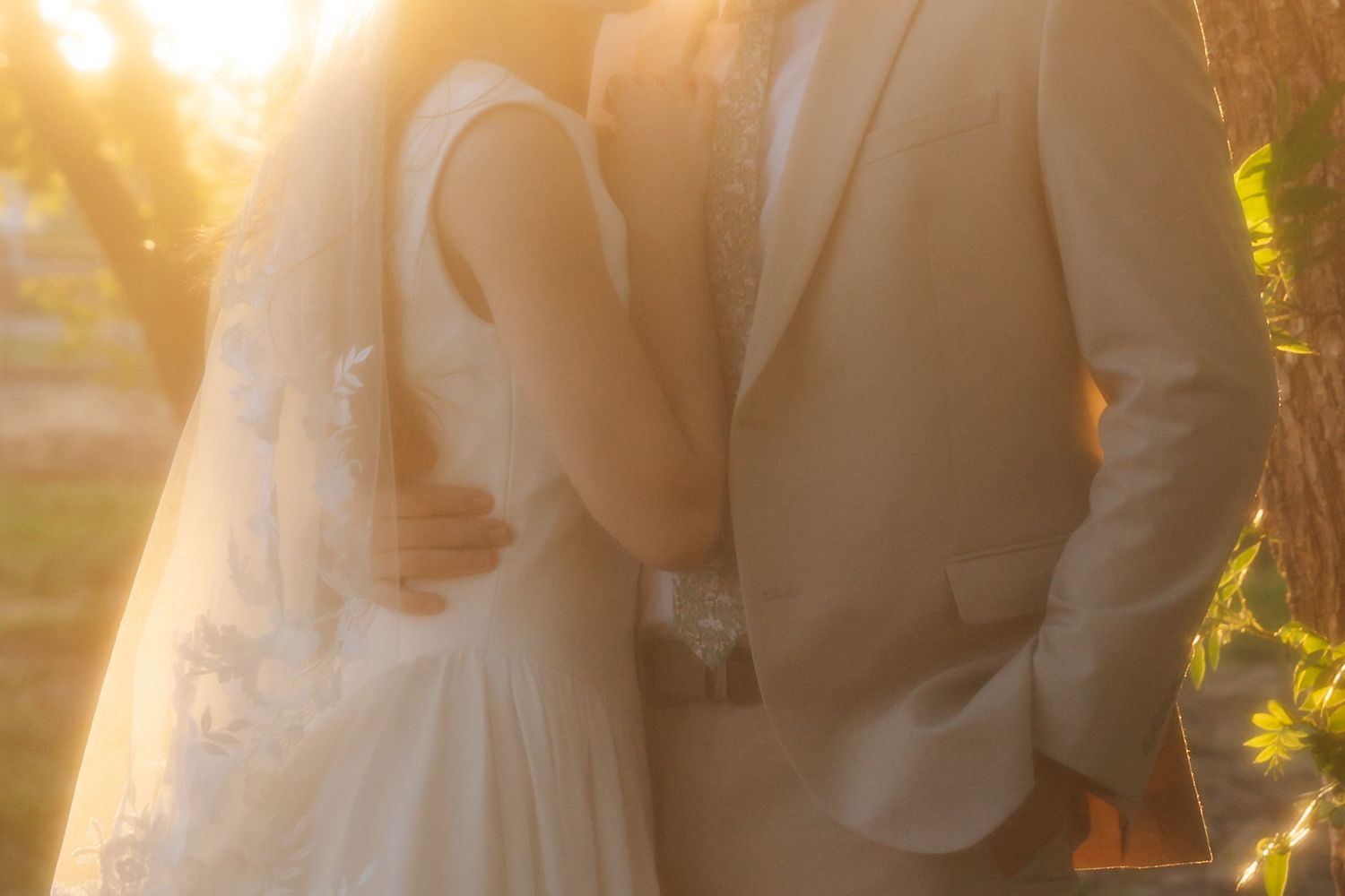 Bride and groom embracing in golden sunset light during outdoor wedding portrait.