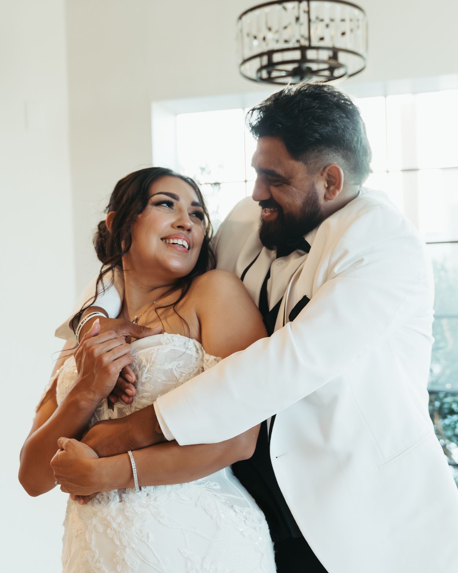 Bride in white lace gown and groom in white jacket share a joyful first dance together.