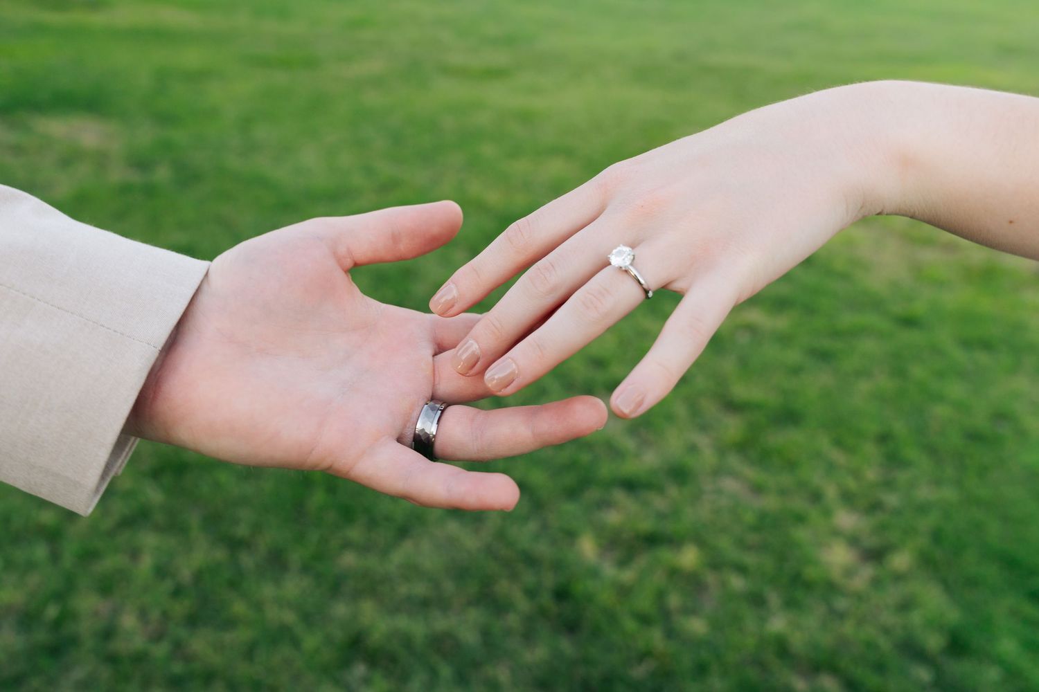 Close-up of bride and grooms hands touching showing their wedding rings on a green grass background.