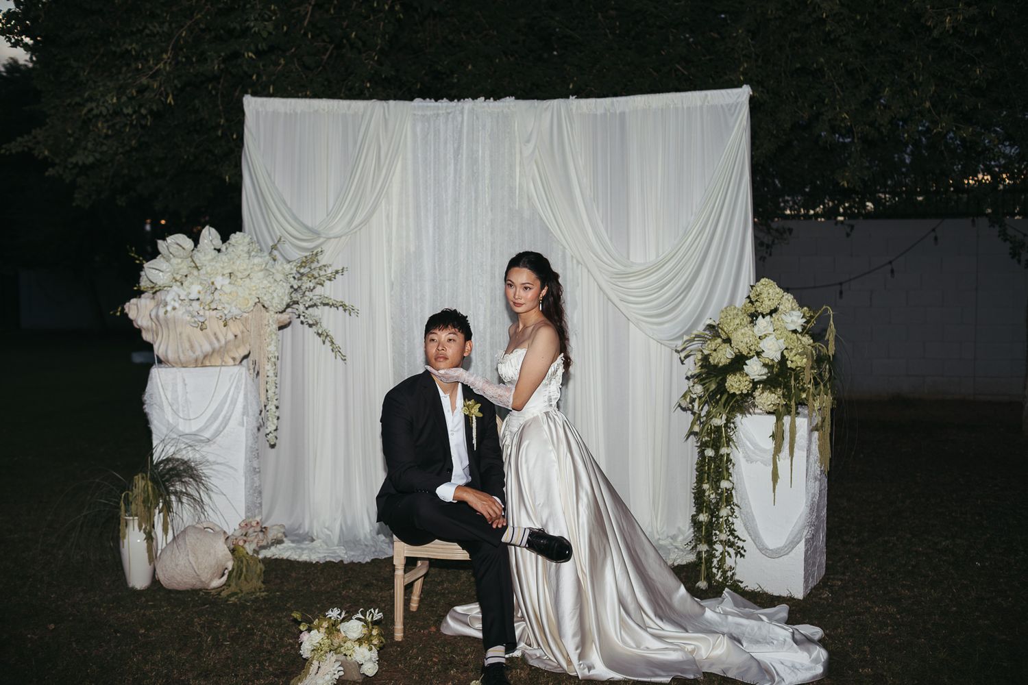 Couple posing at outdoor wedding ceremony with white draped backdrop and elegant floral arrangements.