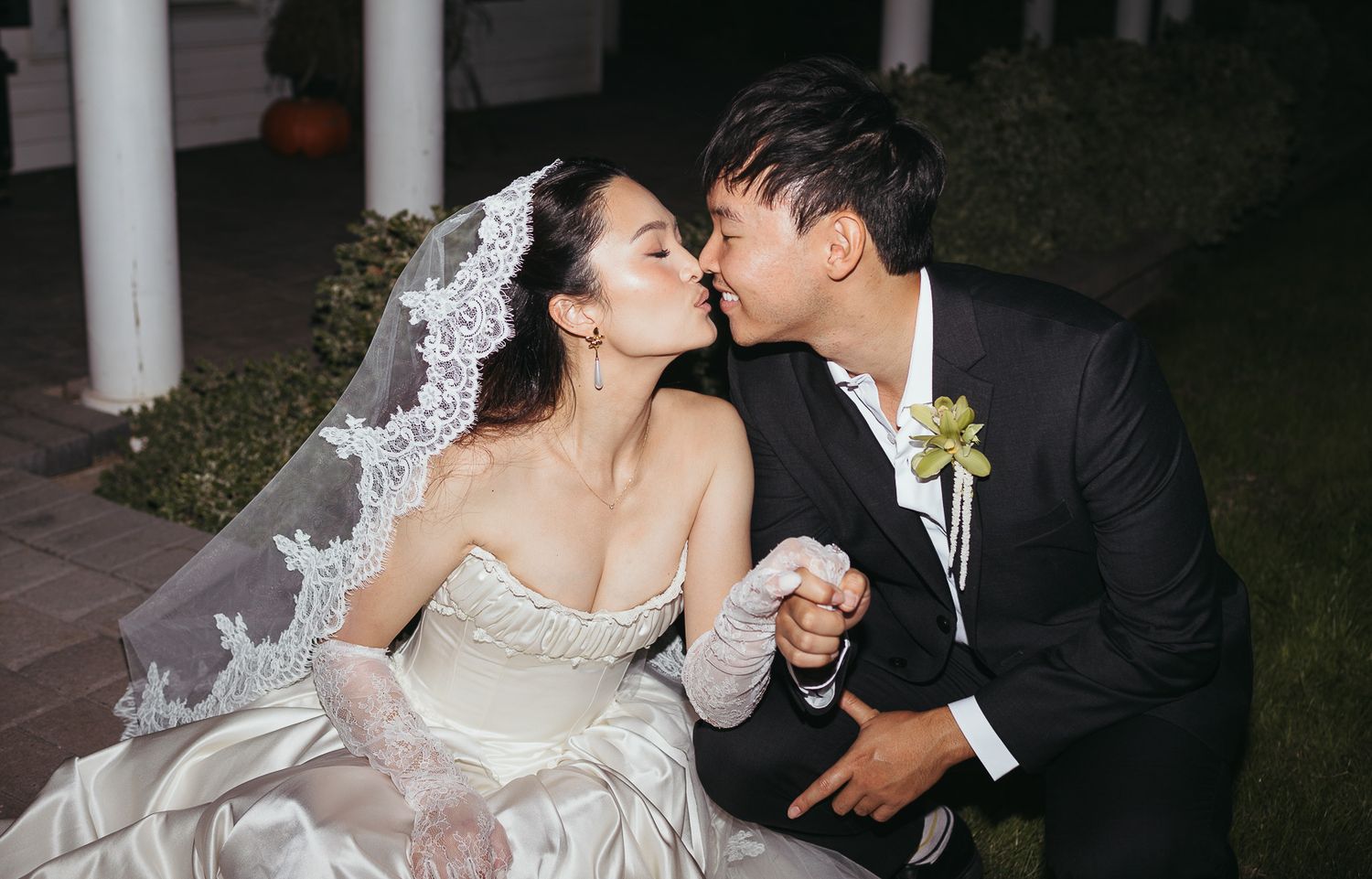Bride and groom kiss while holding hands at night wedding ceremony outdoors.