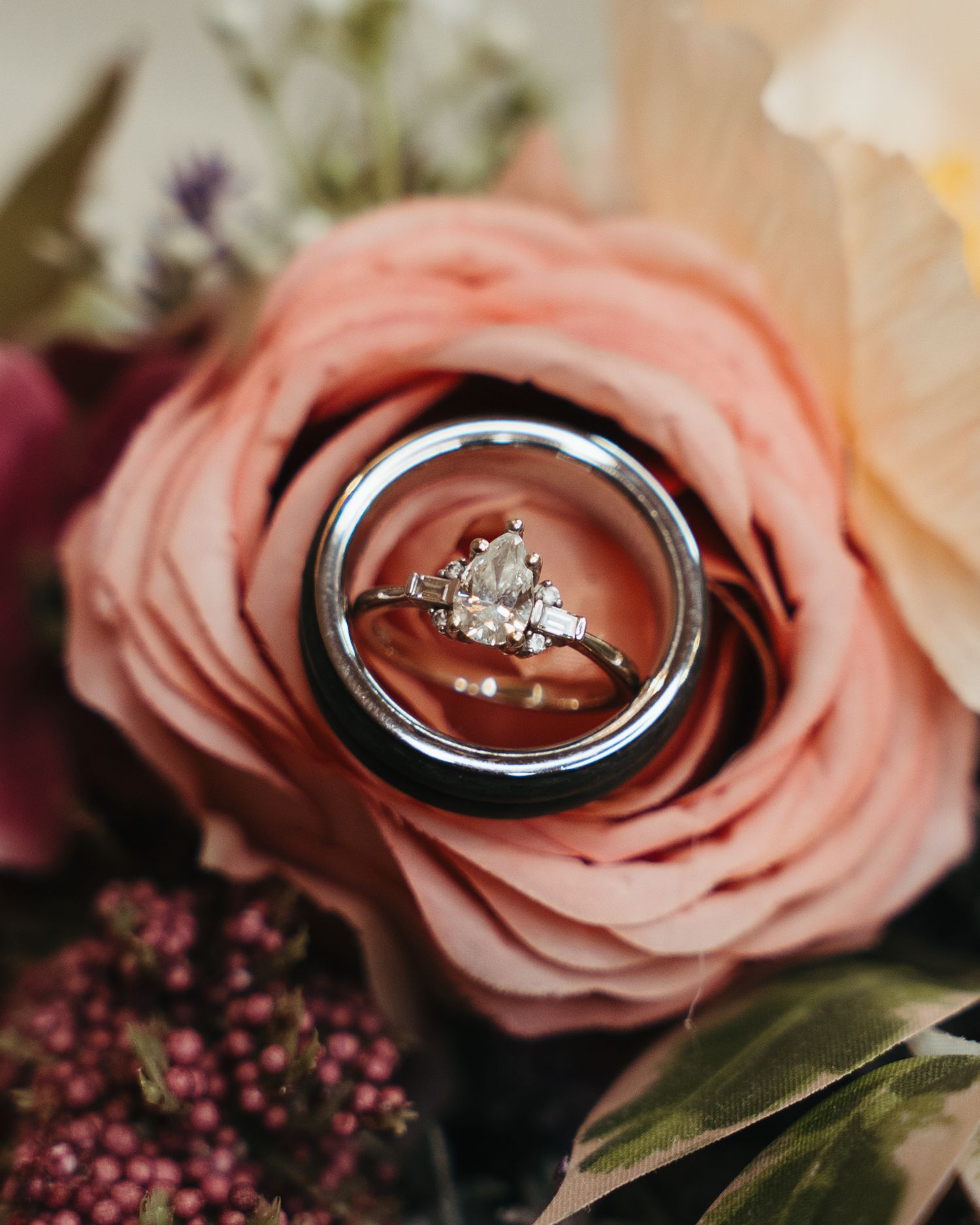 Wedding rings with pear-shaped diamond nestled inside a pink rose with purple flowers.