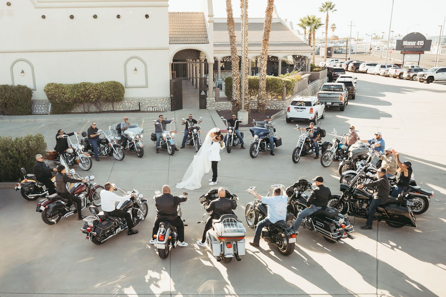 Aerial view of wedding couple surrounded by motorcycles in a circle in a parking lot.