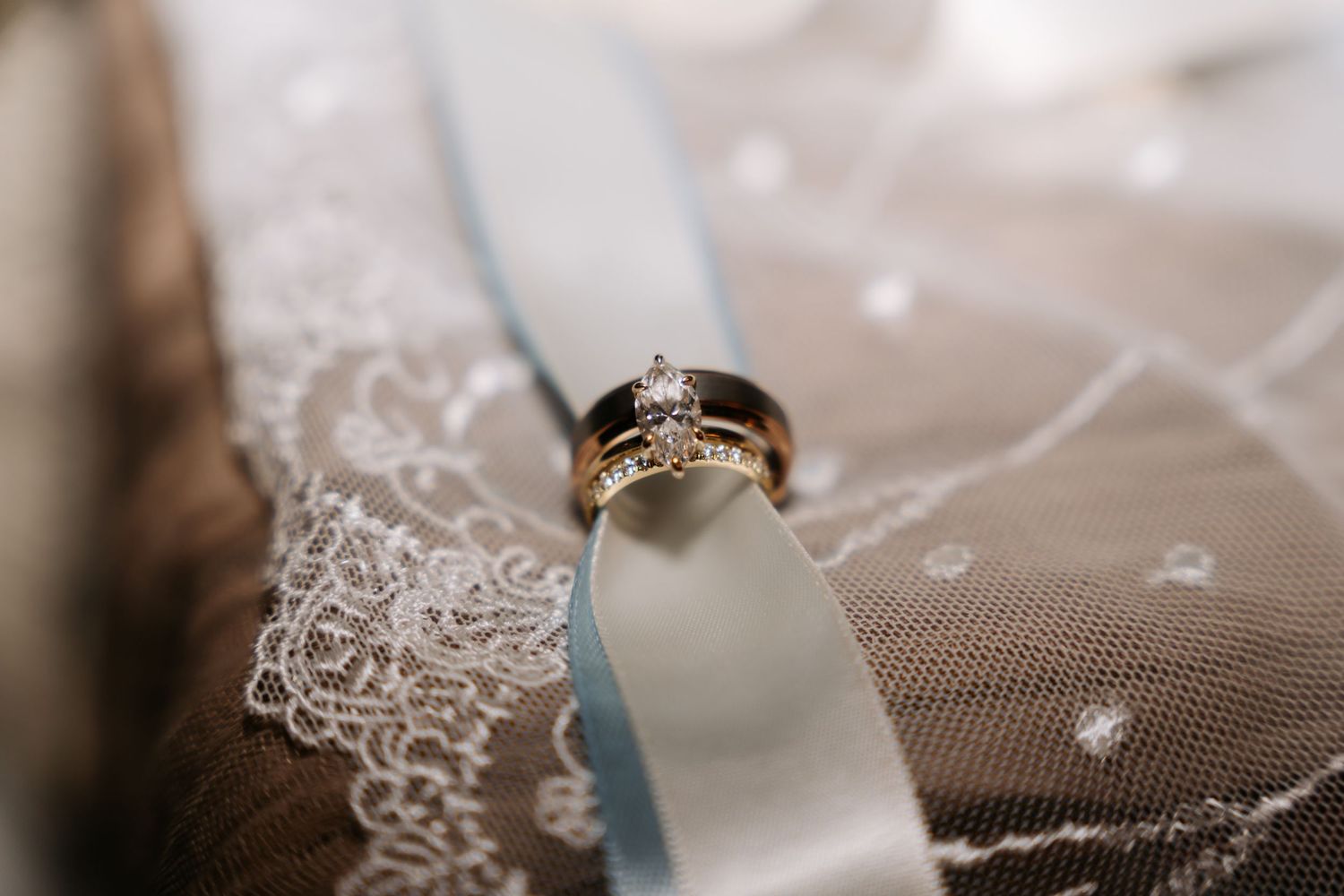 Diamond engagement ring and gold wedding band displayed on lace veil with blue ribbon.
