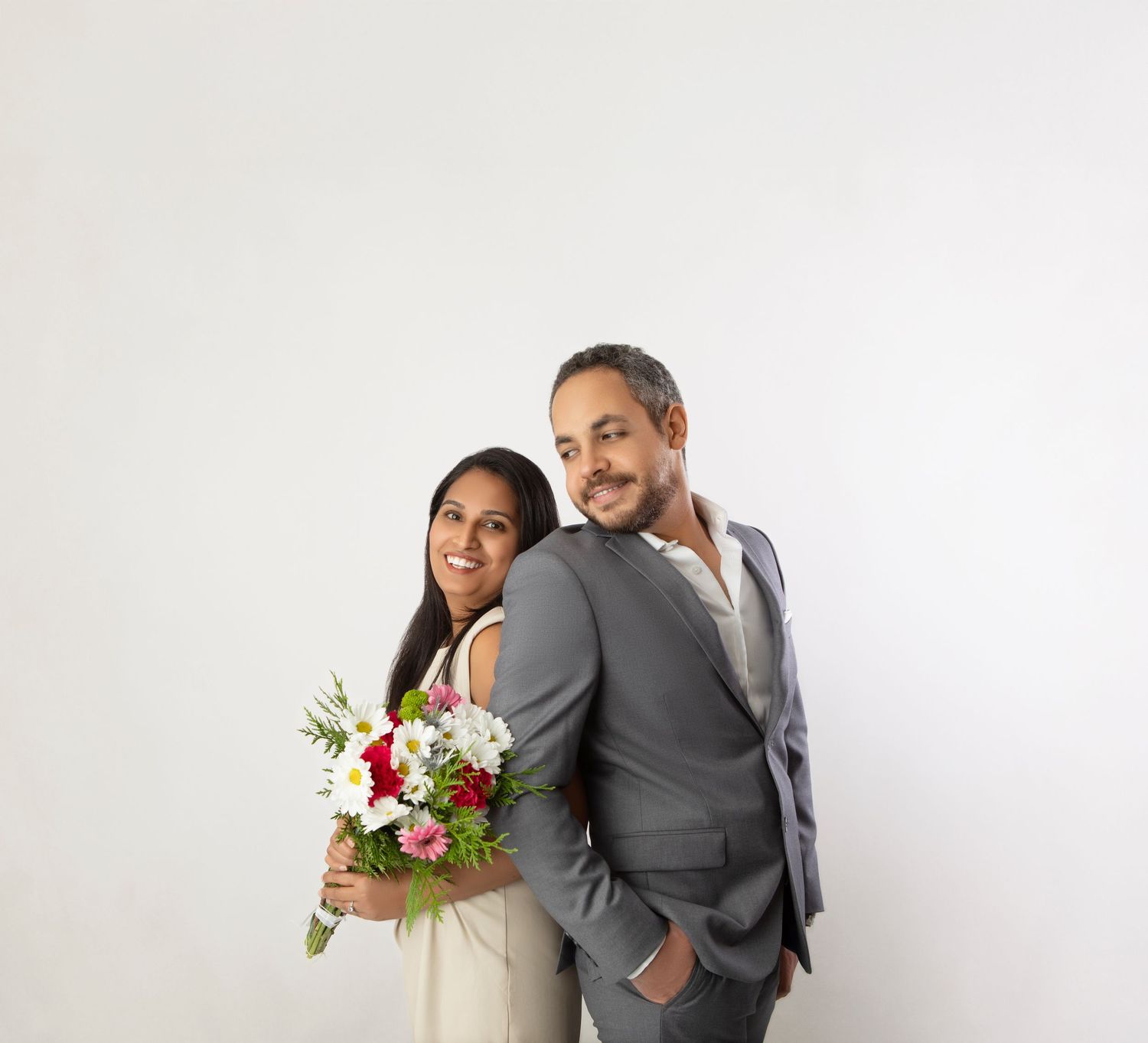 Happy couple posing together with red and white flower bouquet against white studio background.
