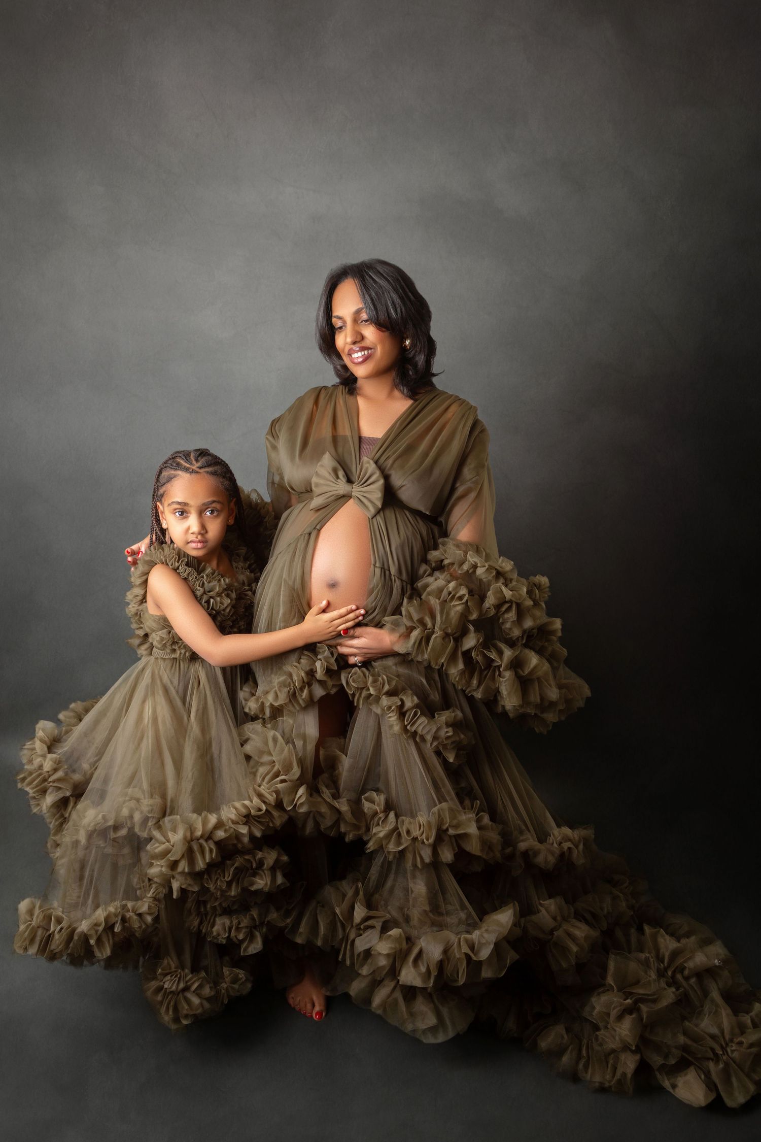 Pregnant woman and daughter pose together in matching olive green ruffle tulle maternity gowns.