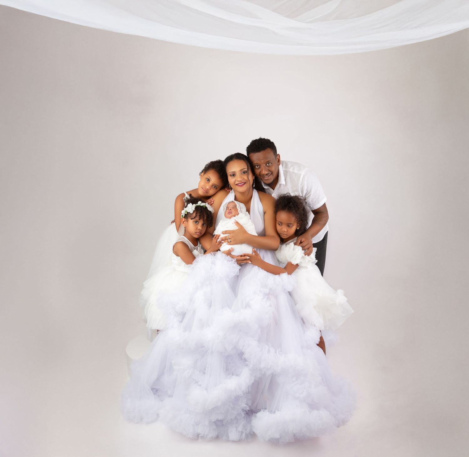 Family of five in white outfits posing with fluffy cloud-like tulle skirt in studio.
