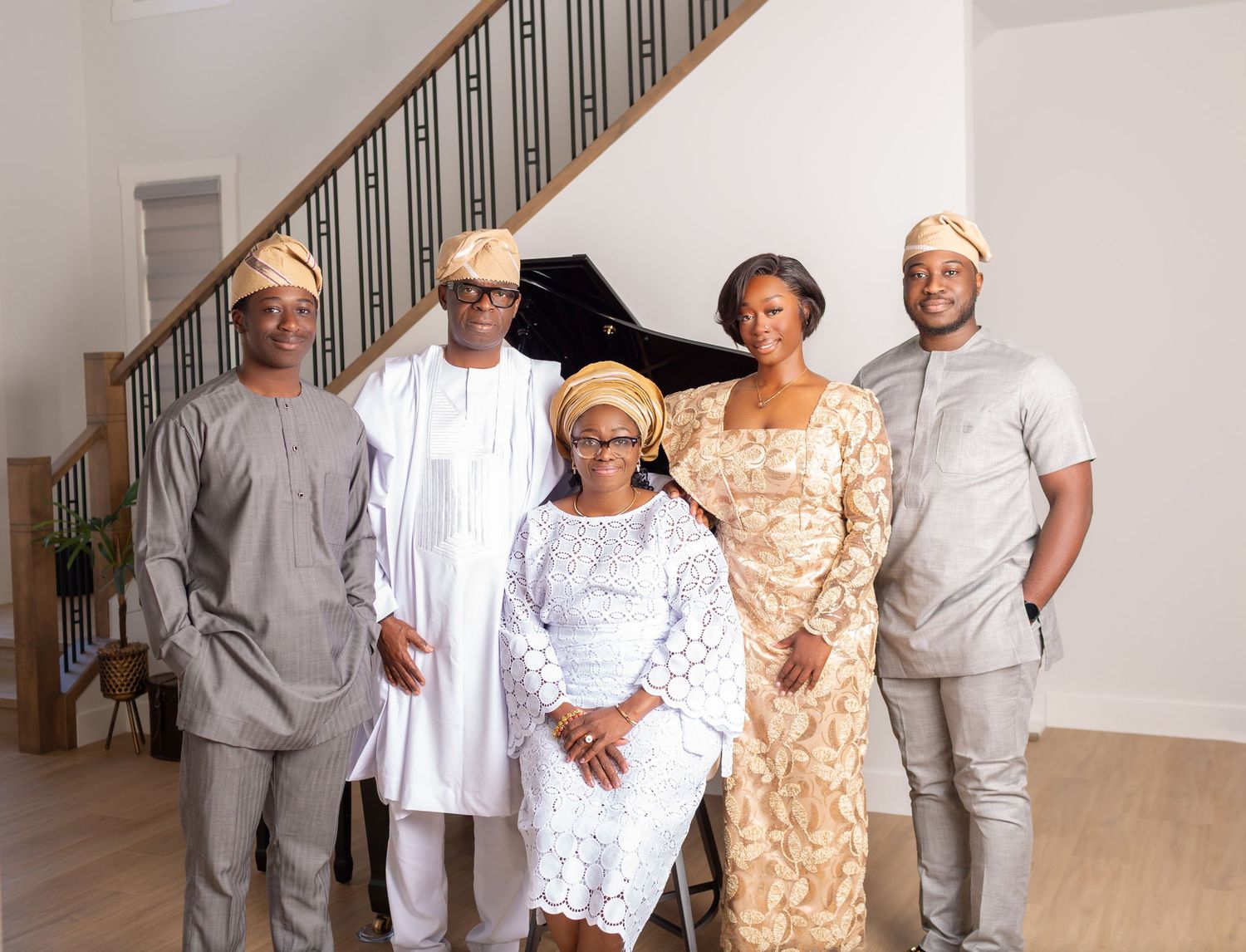 Five family members in traditional Nigerian attire posing near staircase with grand piano.