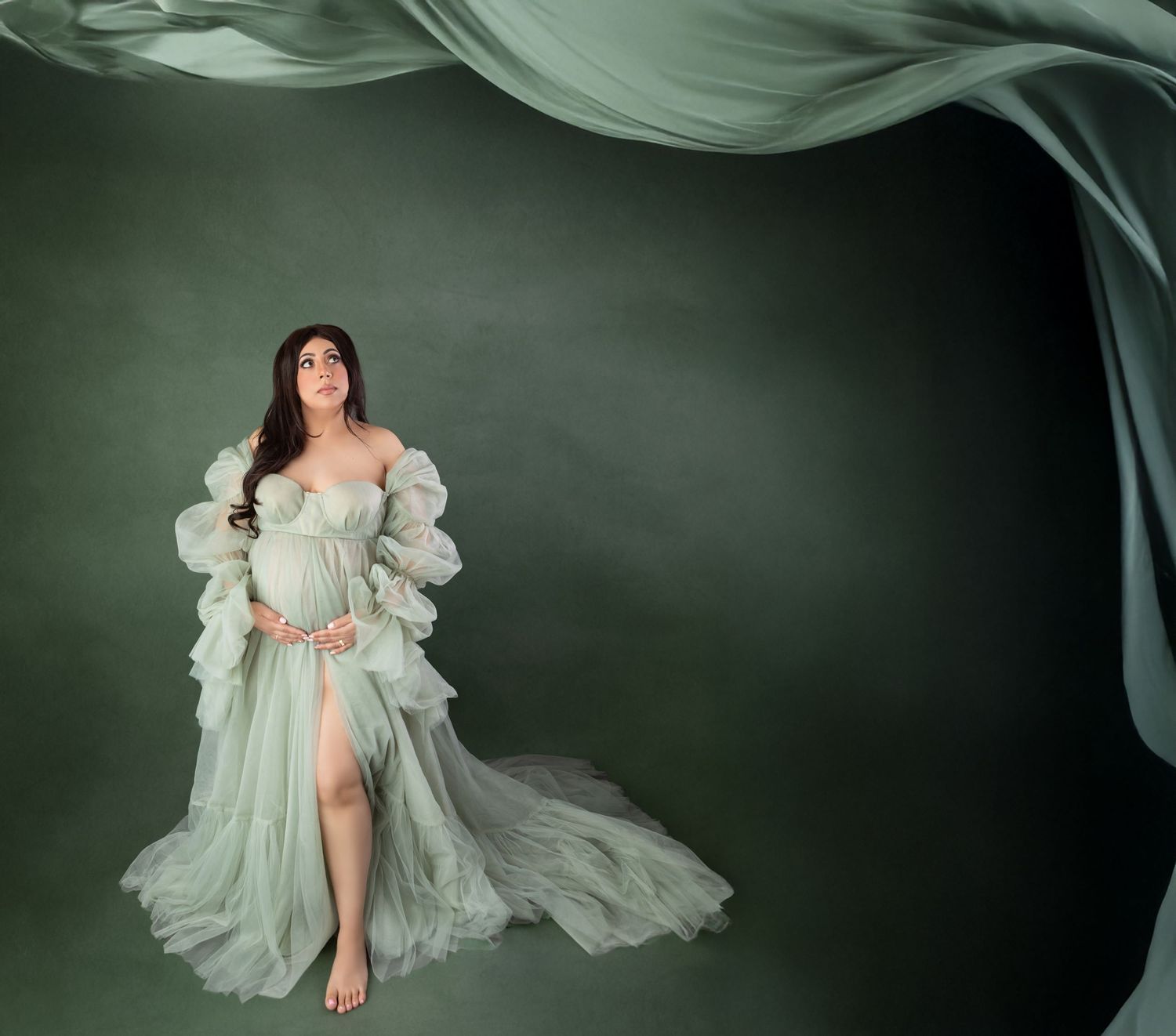 Expectant mother in sage green off-shoulder ruffle maternity dress with flowing fabric.