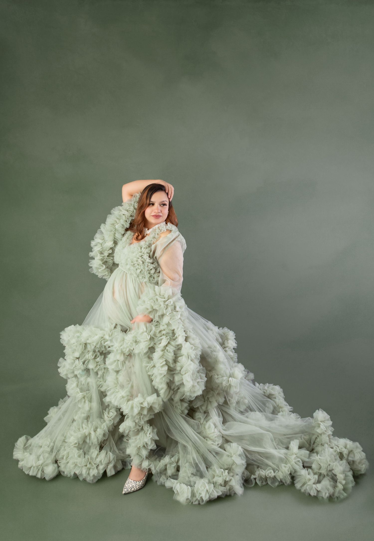 Pregnant woman in elegant sage green ruffled tulle gown posing gracefully in a professional maternity photo shoot.