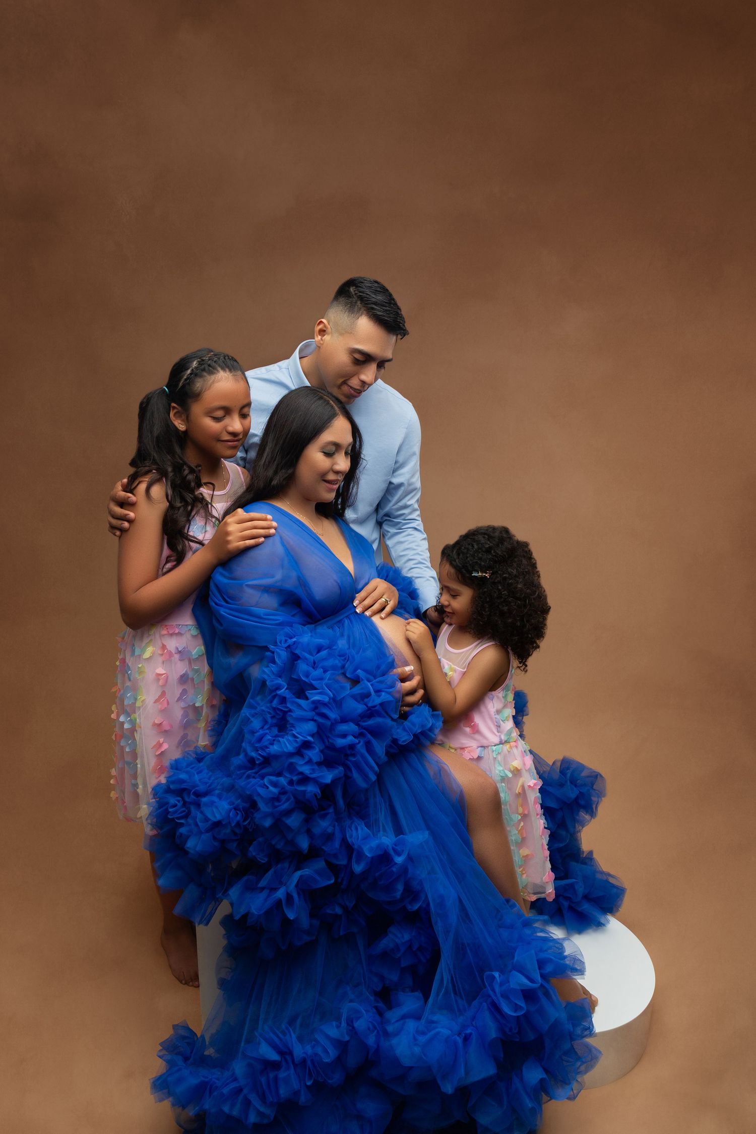 Family maternity portrait with pregnant mom in royal blue tulle gown surrounded by husband and two daughters.