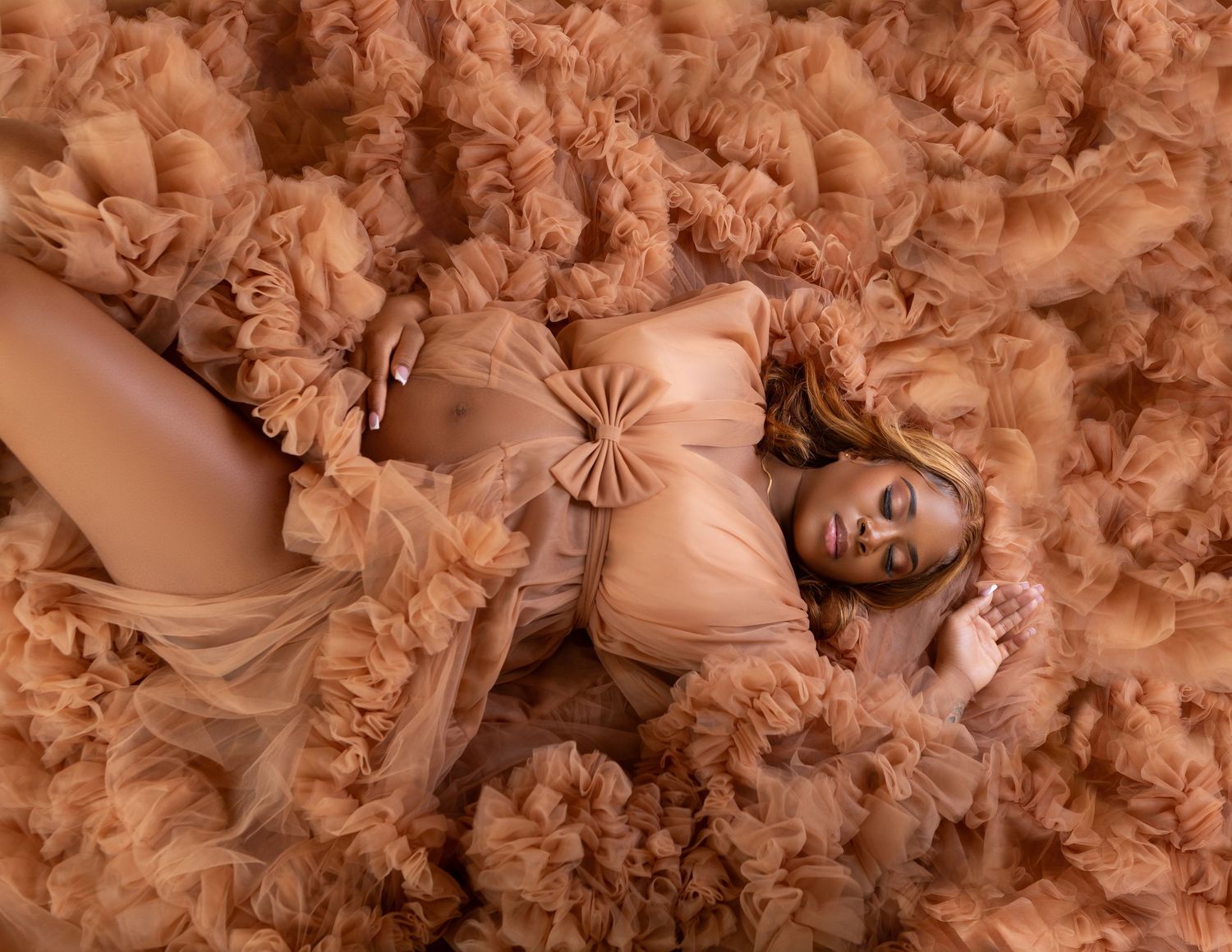 Maternity portrait of woman lying in voluminous caramel tulle fabric from above.