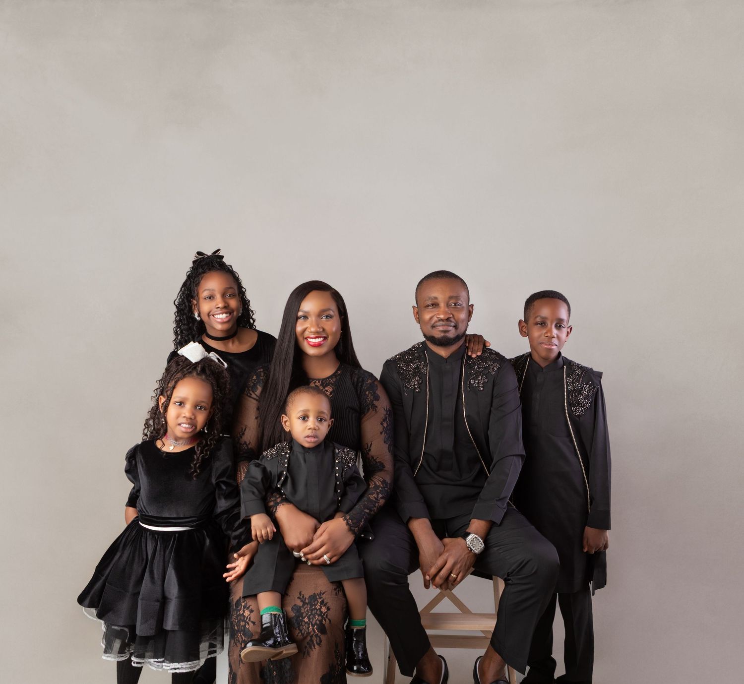 A family of six dressed in black posing together for a professional portrait photo against a gray background.