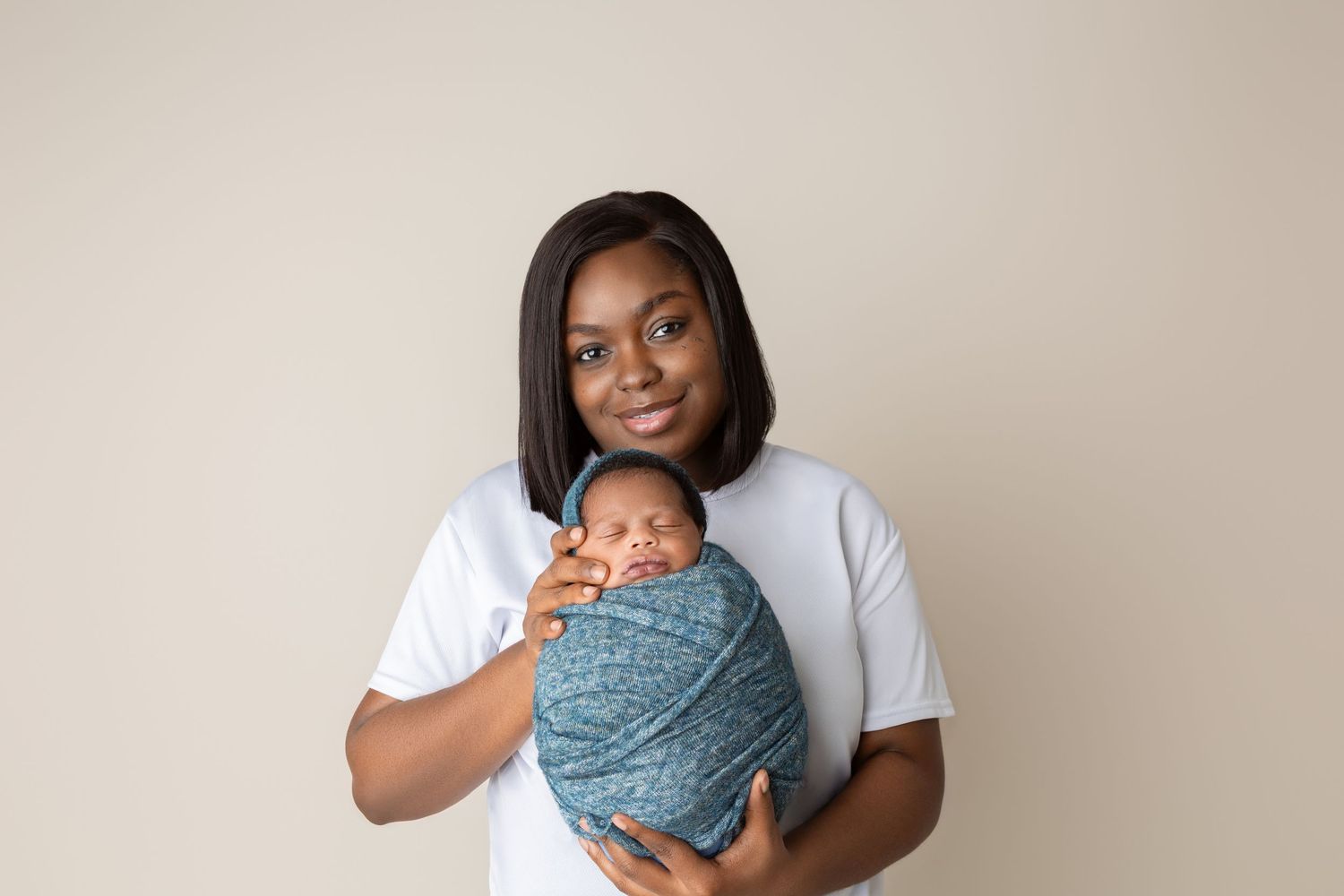 Black mother in white t-shirt holding her swaddled newborn baby in a blue wrap.