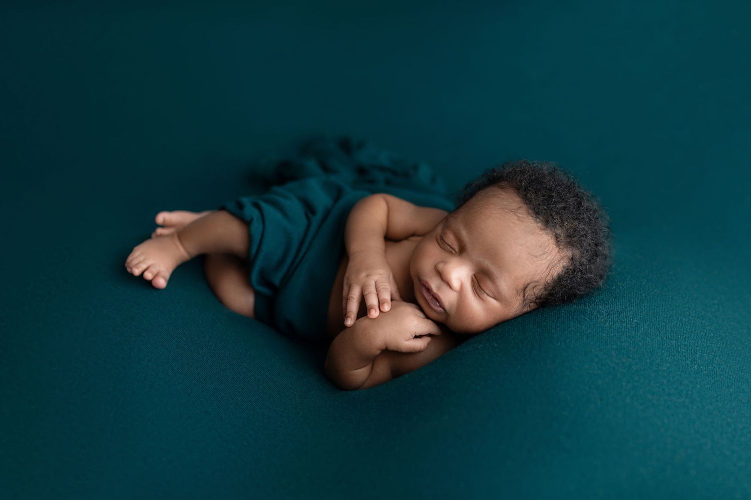 Sleeping newborn baby wrapped in teal fabric on a teal background.