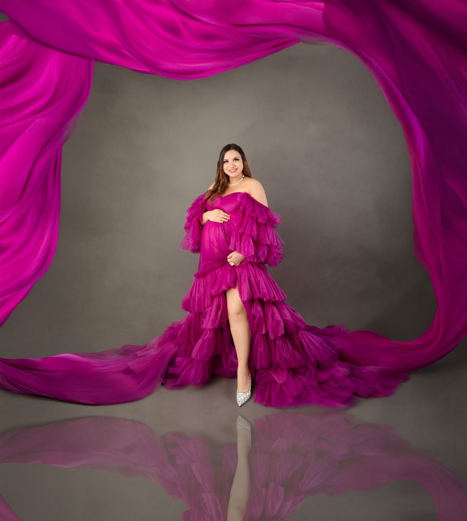 Pregnant woman in stunning magenta ruffled off-shoulder maternity dress with flowing fabric in studio.