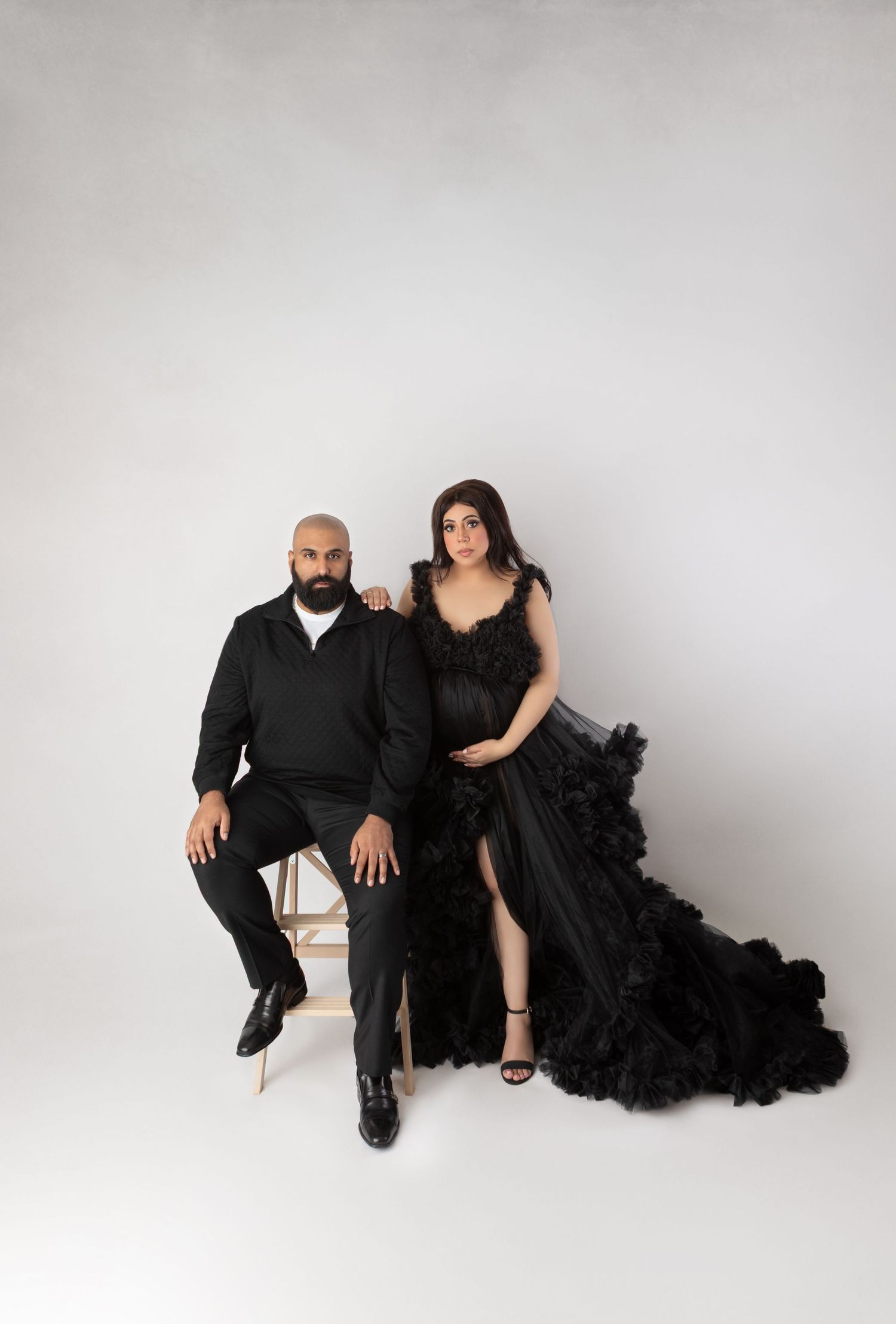 Maternity couple in matching black outfits, woman in dramatic ruffled tulle gown.
